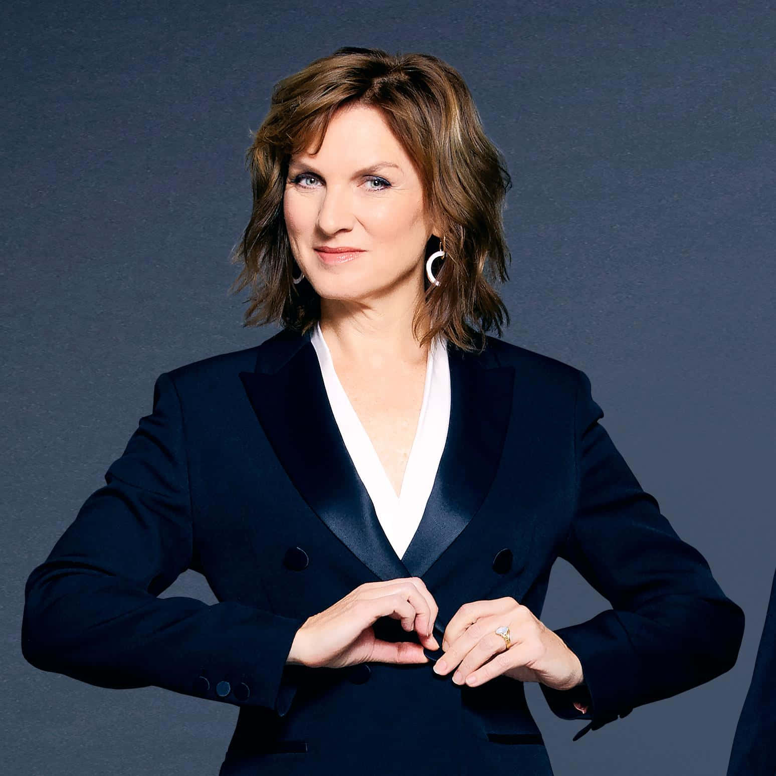 Fiona Bruce 桌布 壁紙 — 一位身穿海軍藍西裝外套和白色襯衫的優雅女性，在柔和的灰色背景下用手比出心形。