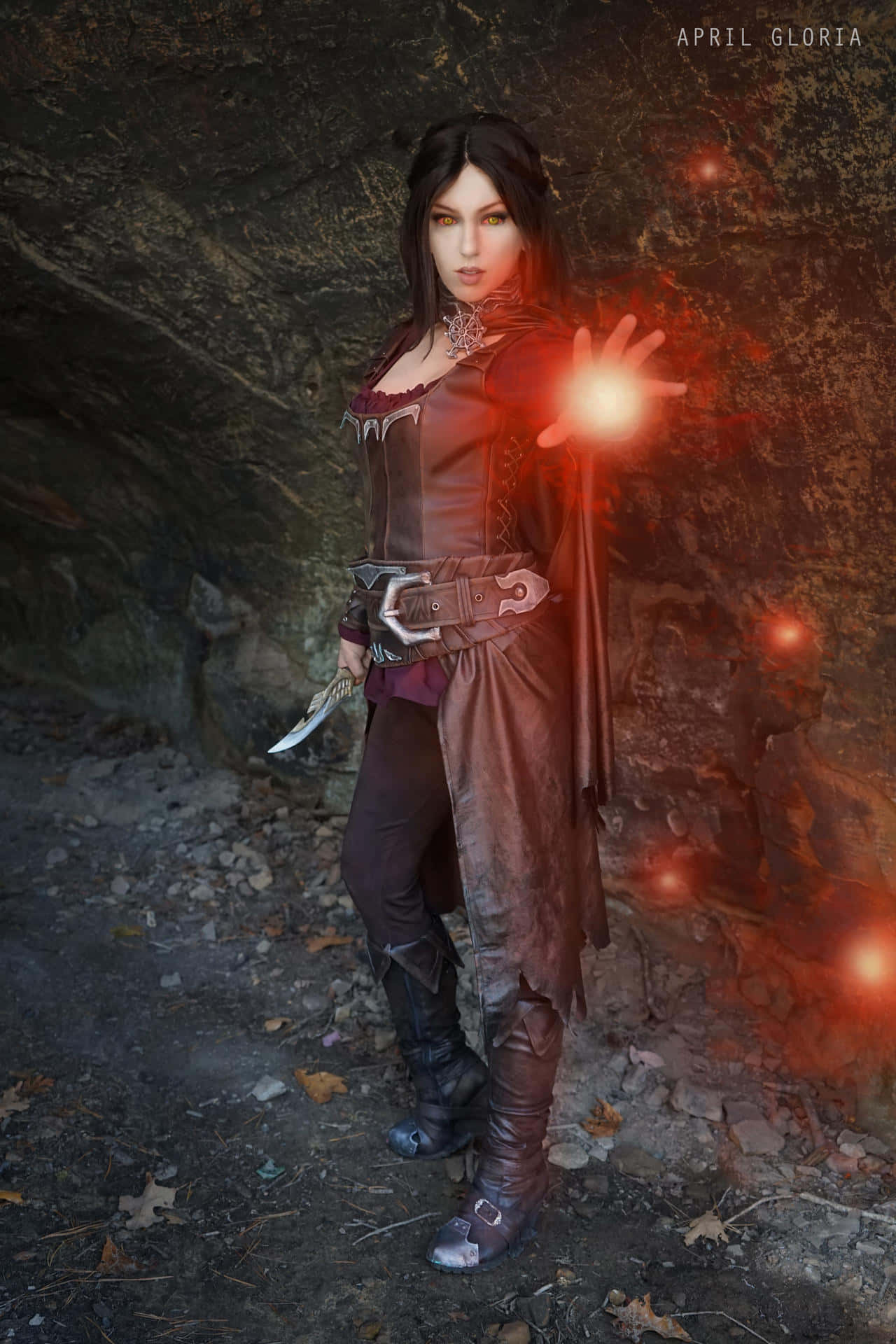 Skyrim Serana 桌布 壁紙 — 一位身穿深色皮甲的奇幻女戰士站在岩石洞穴中，發光的紅色魔法從她伸出的手中噴湧而出。