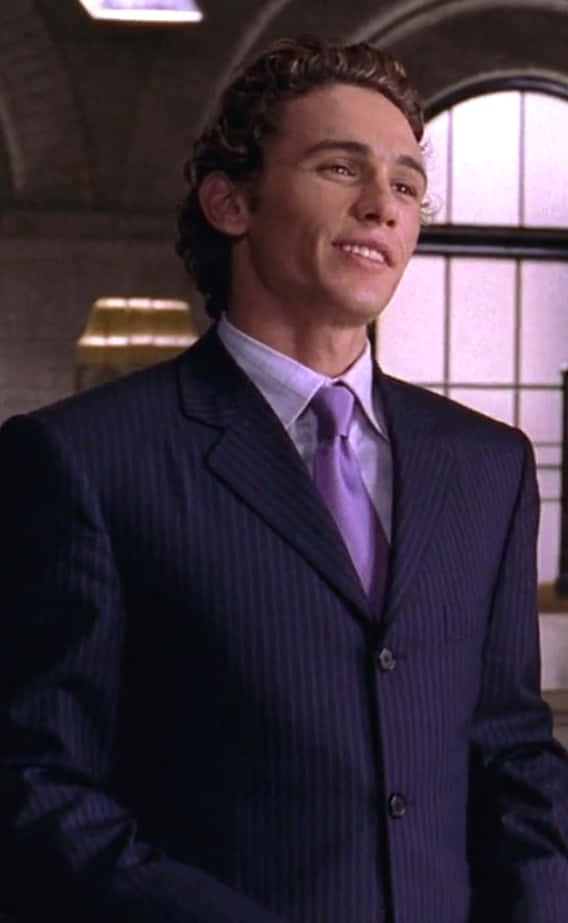 Harry Osborn 桌布 壁紙 — 一位身穿深色細條紋西裝和紫色領帶的年輕男子，在拱形窗戶的柔和光線室內環境中溫暖地微笑。
