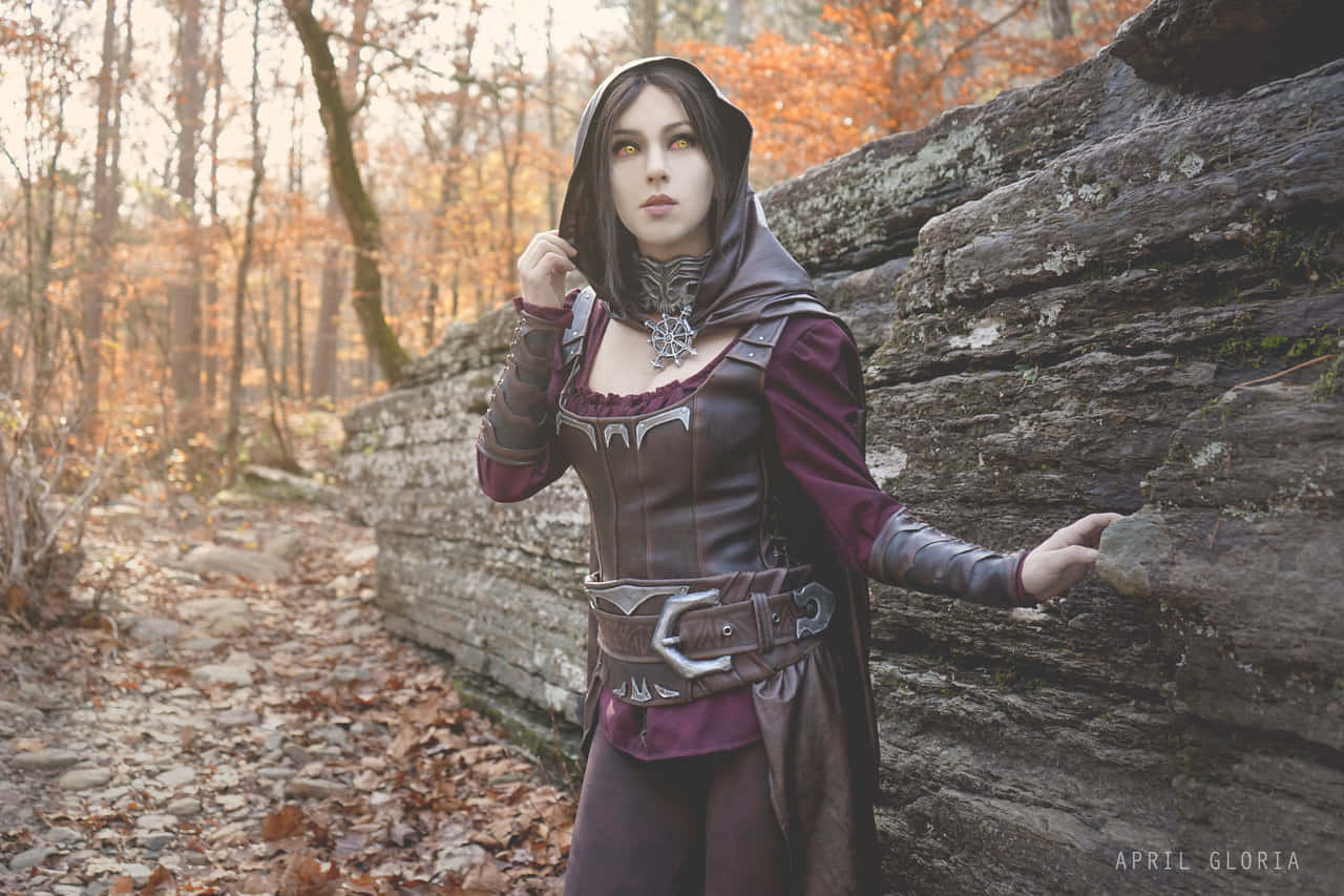 Skyrim Serana 桌布 壁紙 — 一位身穿深色連帽奇幻服裝的女性站在秋日森林中長滿苔蘚的石牆旁，周圍是金色的樹葉。