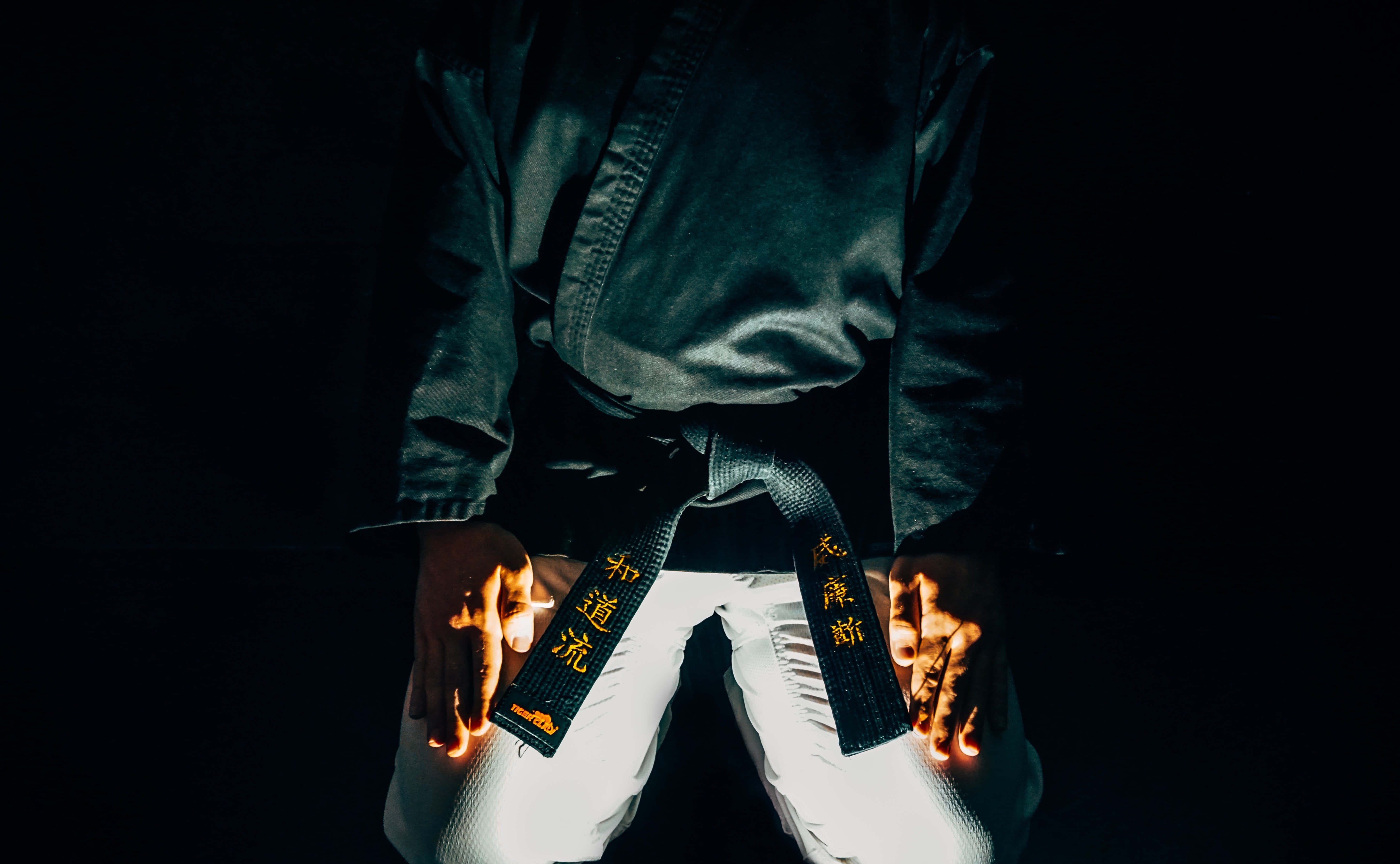 Martial Arts Uniform 桌布 壁紙 — 一位身穿深色道服的武術家，在漆黑背景下用發光的雙手握著一條黑帶。