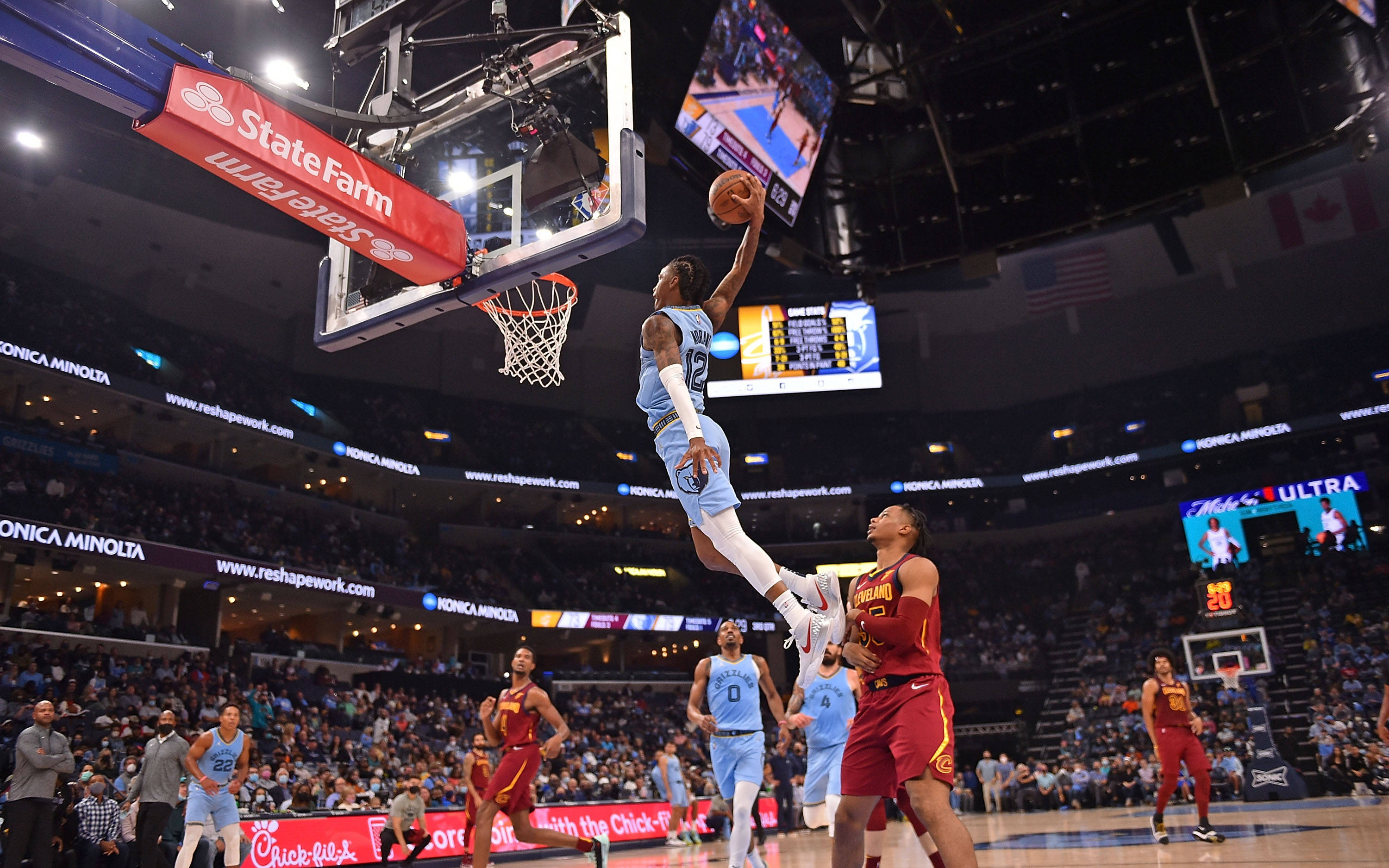 Cleveland Cavaliers 桌布 壁紙 — 一位身穿淺藍色球衣的籃球運動員在空中飛翔，完成一次強力入樽，防守球員在擠滿觀眾的場館下方觀看。