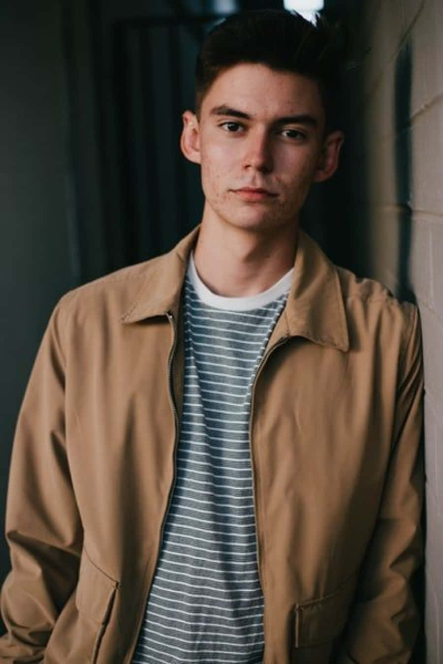 Boy 桌布 壁紙 — 一位身穿淺褐色外套和條紋襯衫的年輕男子，表情嚴肅地靠在牆上。