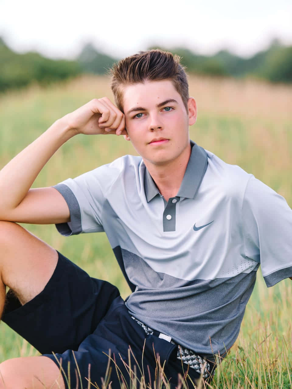 Boy 桌布 壁紙 — 一位身穿灰色Nike Polo衫的年輕男子，在陽光明媚、樹木環繞的草地上若有所思地坐著。