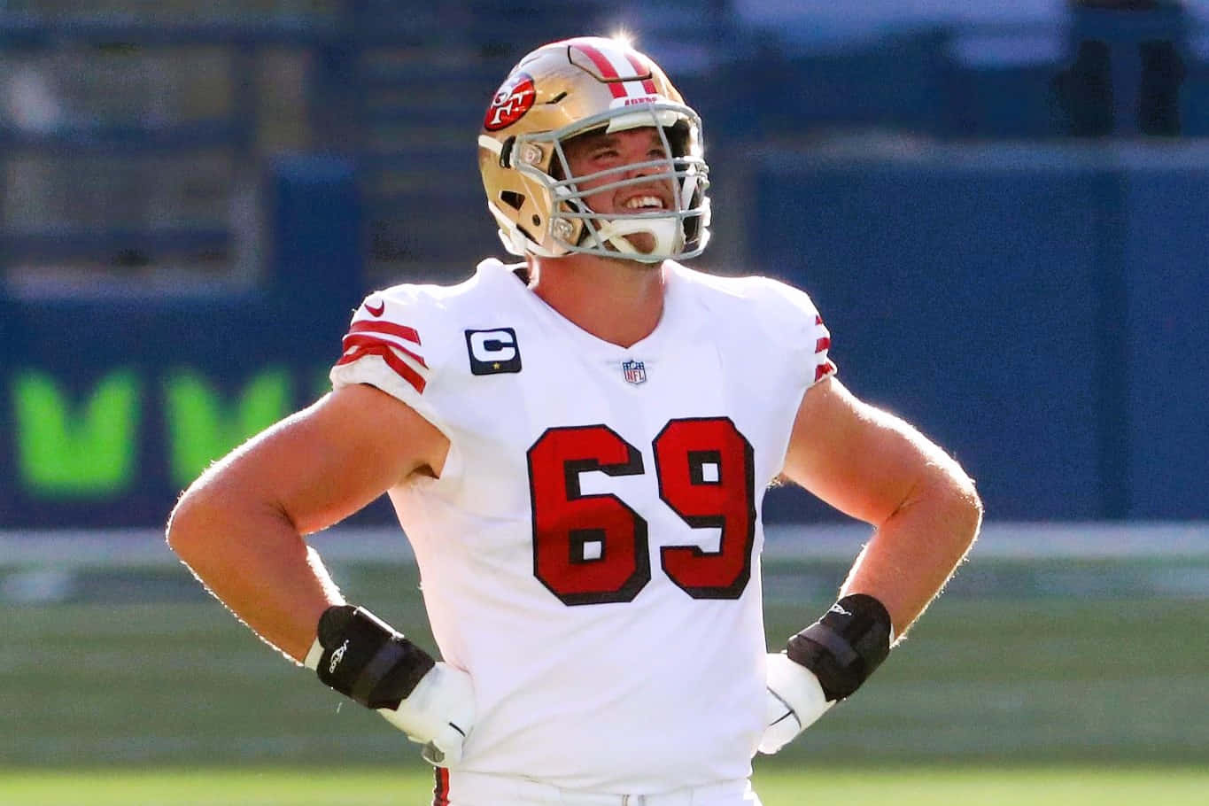 Mike Mcglinchey 桌布 壁紙 — 一位身穿白色69號球衣的三藩市49人美式足球員，自信地站在陽光明媚的球場上，雙手叉腰。