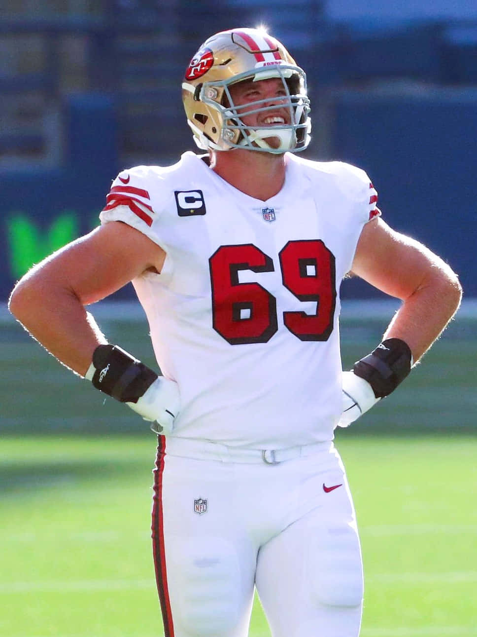 Mike Mcglinchey 桌布 壁紙 — 一位身穿白色69號球衣的舊金山49人隊美式足球員，在陽光明媚的球場上自信地雙手叉腰站立。