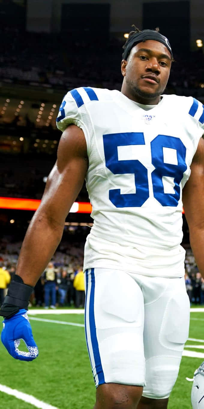 Bobby Okereke 桌布 壁紙 — 一位身穿白色和藍色球衣、號碼58的專注足球員，在球場燈光下站在明亮的綠色場地上。