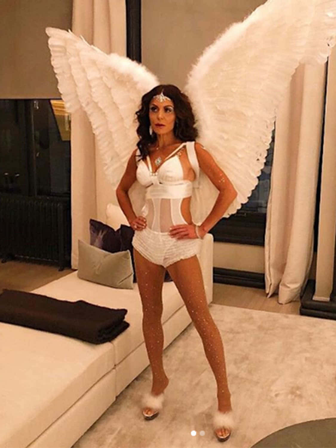 Victoria's Secret 桌布 壁紙 — 一位身穿白色天使服裝、擁有大型羽毛翅膀的女性在現代客廳中自信地擺姿勢。
