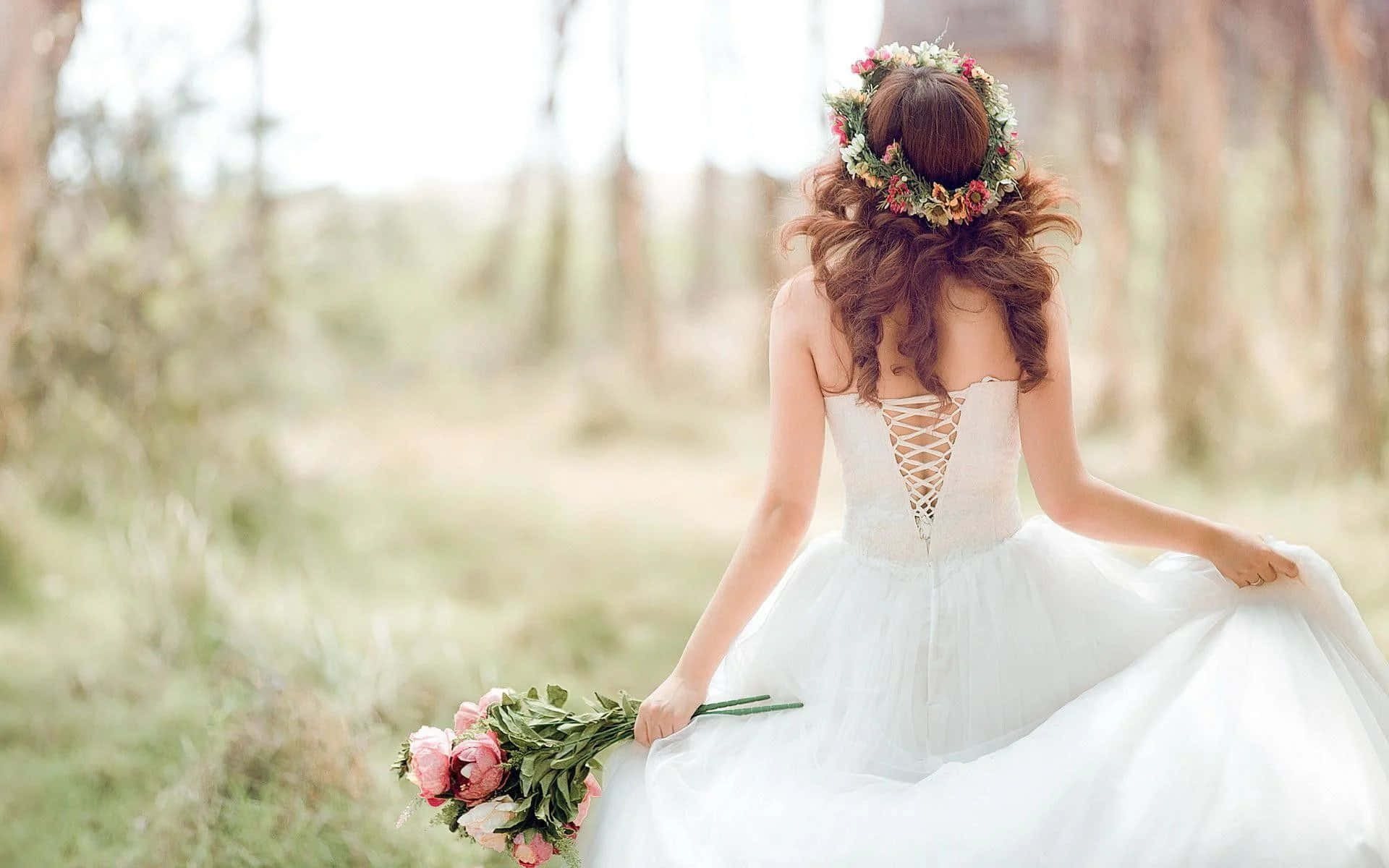 Wedding Dress 桌布 壁紙 — 一位身穿白色婚紗、頭戴花冠的新娘，手持粉紅玫瑰束，走過陽光普照的森林。