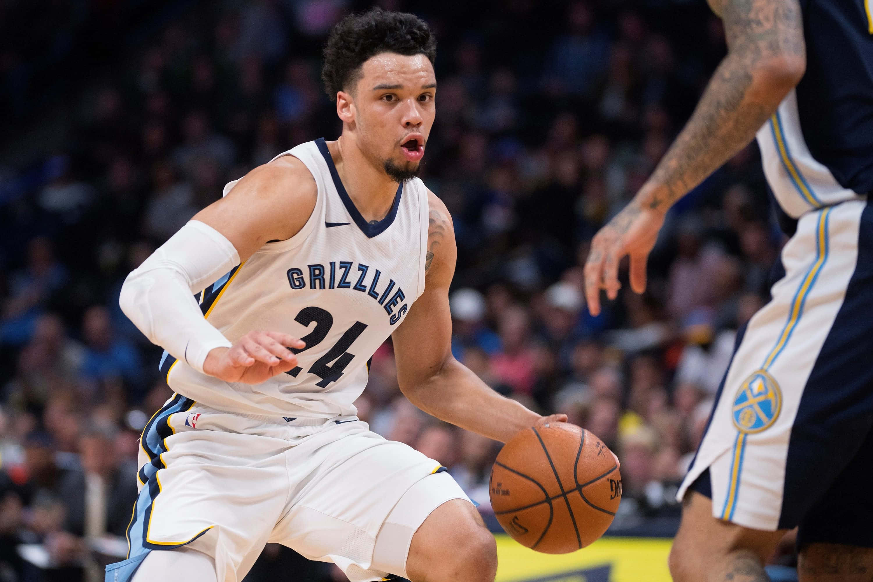 Dillon Brooks 桌布 壁紙 — 一位身穿白色灰熊隊球衣的專注籃球運動員在燈光明亮的場館中運球，同時被防守。