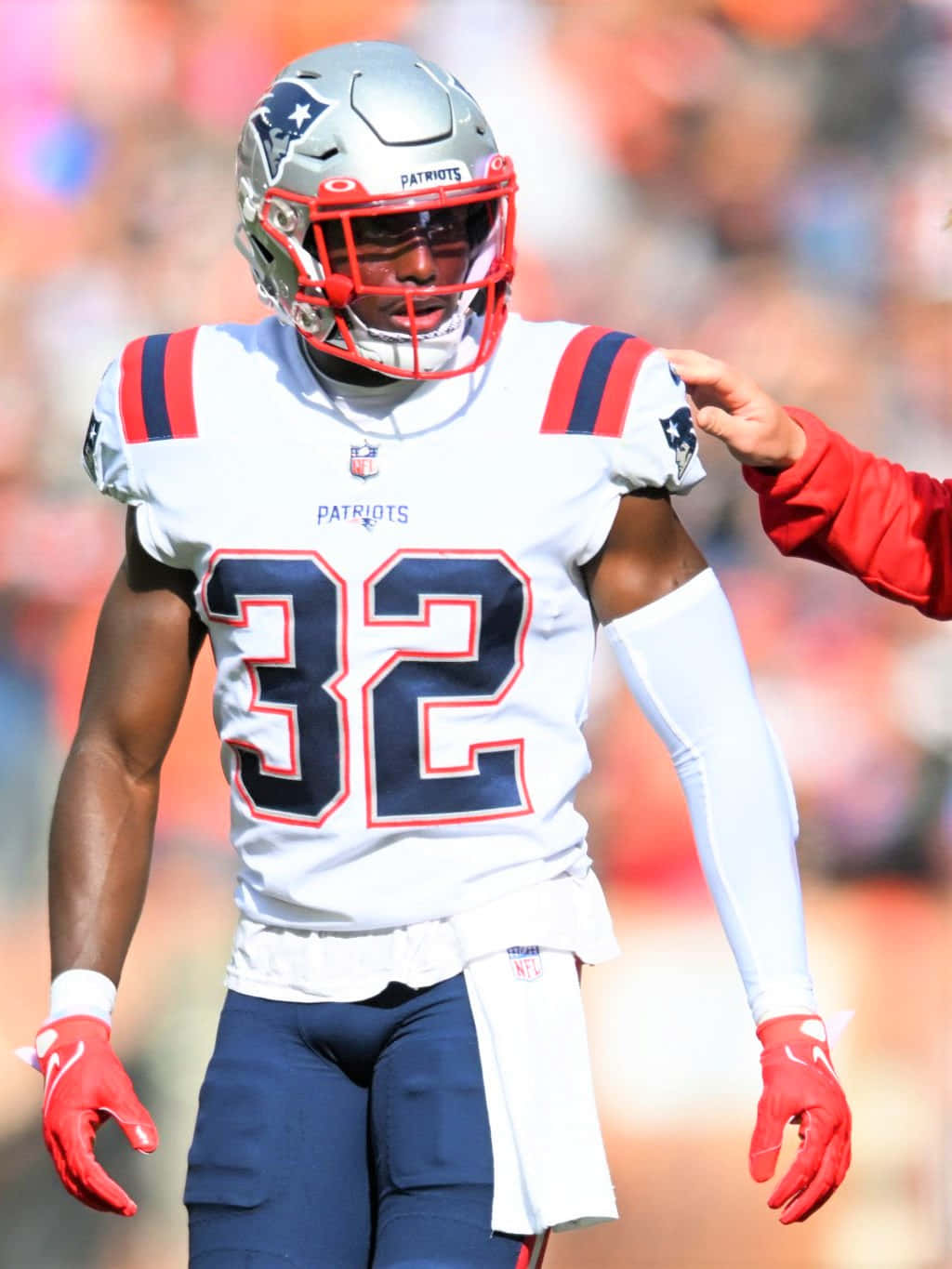 Devin Mccourty 桌布 壁紙 — 一位身穿白色球衣32號的新英格蘭愛國者隊美式足球員，在陽光照耀的球場上行走，一手放在肩膀上。