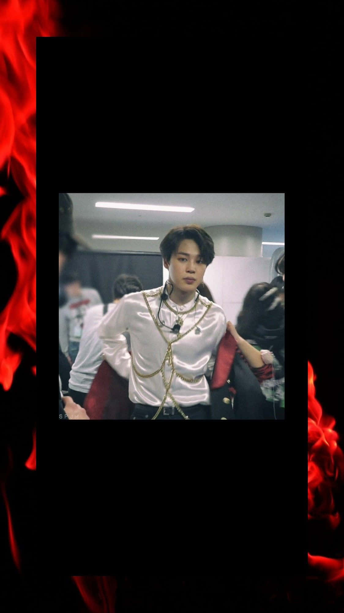 Jimin Aesthetic 桌布 壁紙 — 一位身穿白色緞面襯衫和金色鏈條的年輕男子自信地站在熾熱的紅色火焰邊框前。