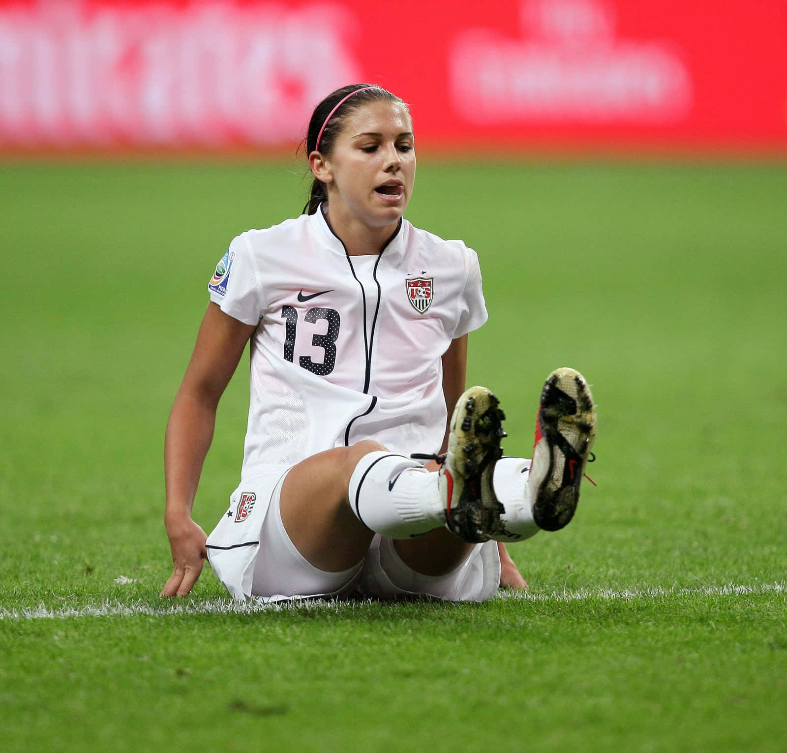 Alex Morgan 桌布 壁紙 — 一位身穿白色美國球衣的女足球員在比賽後坐在充滿活力的綠色球場上，雙腿抬起。