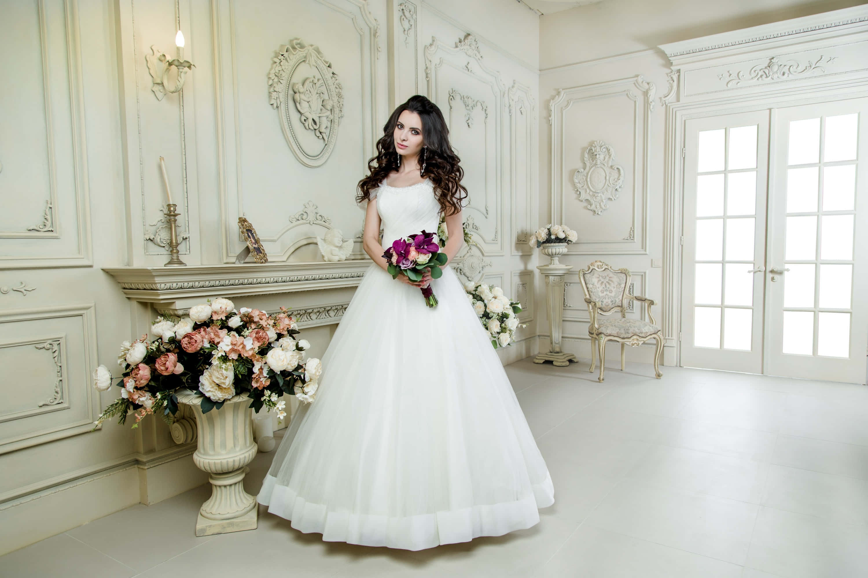 Wedding Dress 桌布 壁紙 — 一位身穿白色蓬鬆婚紗的新娘，在一個裝飾華麗的奶油色房間裡，手持一束粉白相間的花束，房間內有精緻的線條裝飾和法式門。