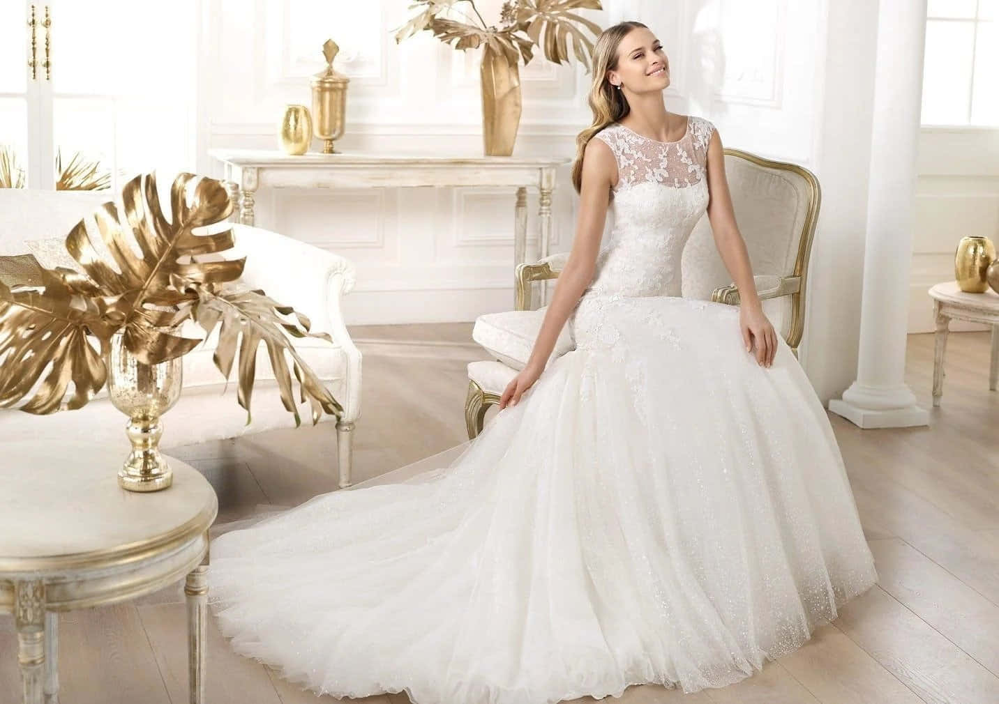 Wedding Dress 桌布 壁紙 — 一位身穿白色蕾絲婚紗的新娘優雅地坐在一間陽光充足、帶有金色裝飾和龜背竹葉的華麗房間裡。