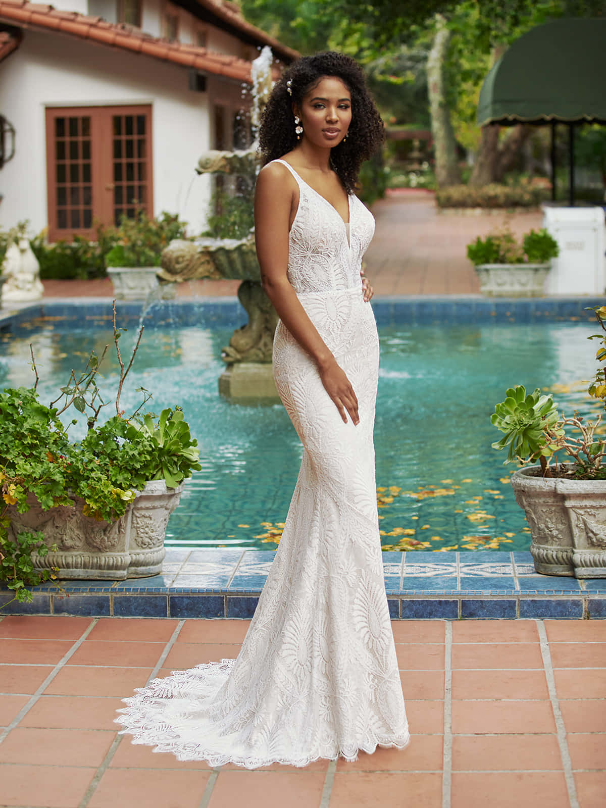 Bride's Dress 桌布 壁紙 — 一位身穿白色蕾絲美人魚婚紗的女性，優雅地站在碧藍的泳池旁，周圍環繞著茂密的綠植和赤陶磚。