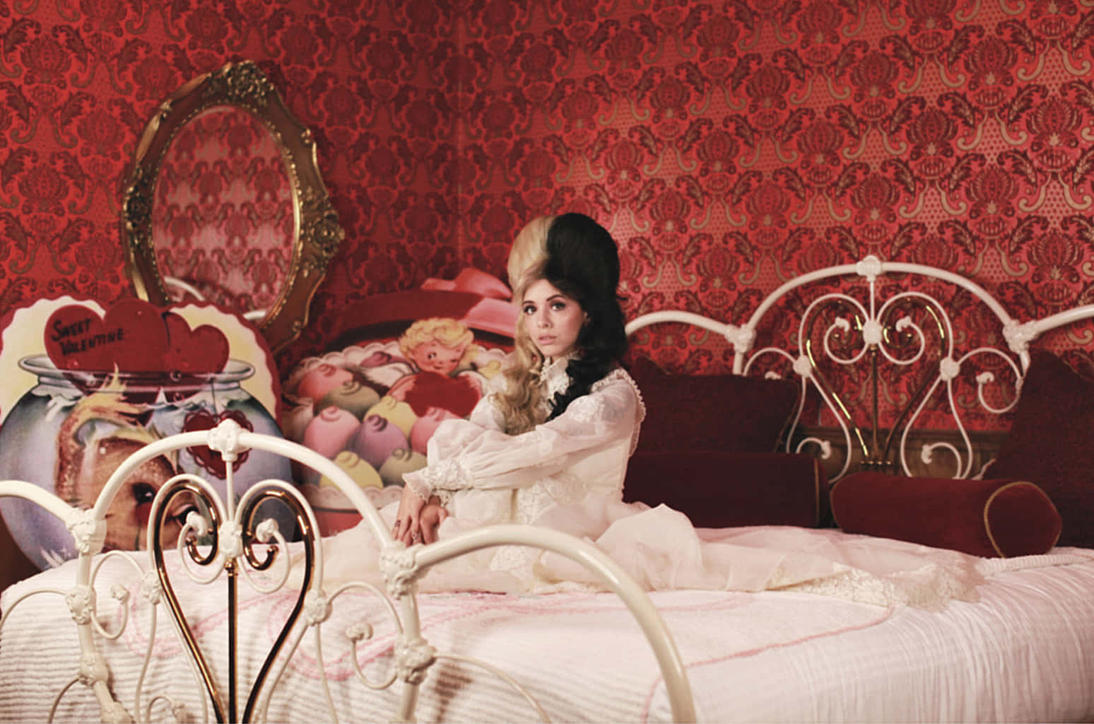Melanie Martinez 桌布 壁紙 — 一位身穿白色蕾絲連衣裙的女性坐在裝飾華麗的床上，房間內有紅色錦緞牆紙和復古裝飾。