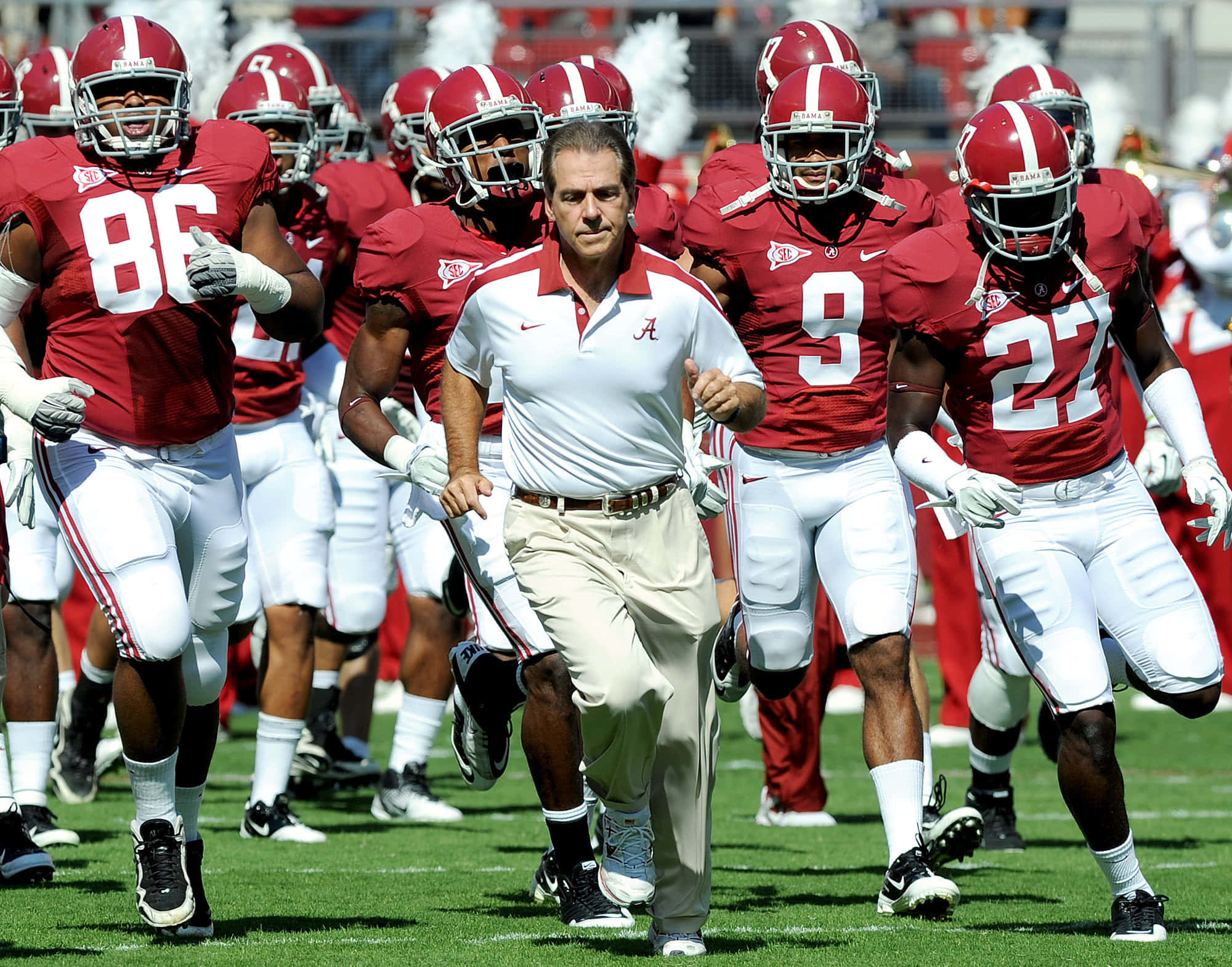 Roll Tide! 壁紙 — 一位身穿白色衣服的足球教練在陽光明媚的綠色球場上與他的紅白球隊一起奔跑。