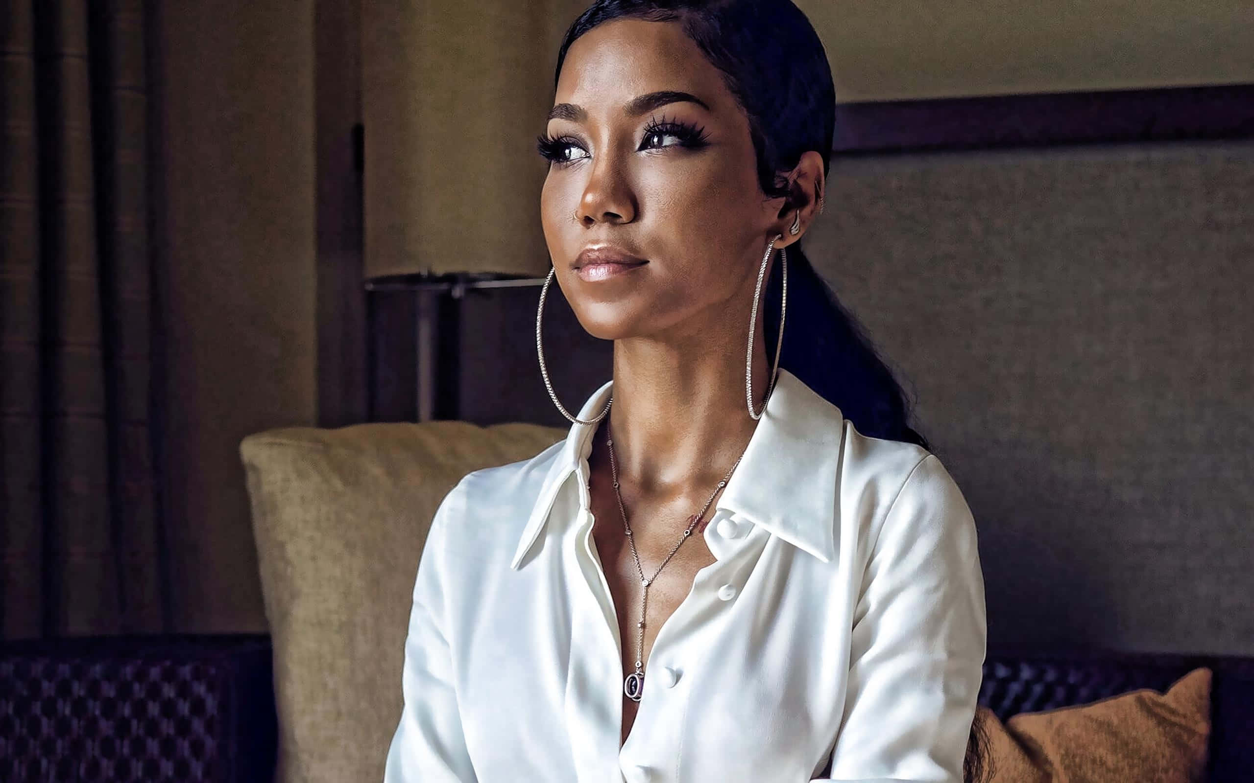 jhene aiko 桌布 壁紙 — 一位身穿白色襯衫、戴著大圈耳環的優雅女士，在豪華酒店房間裡若有所思地凝視著。