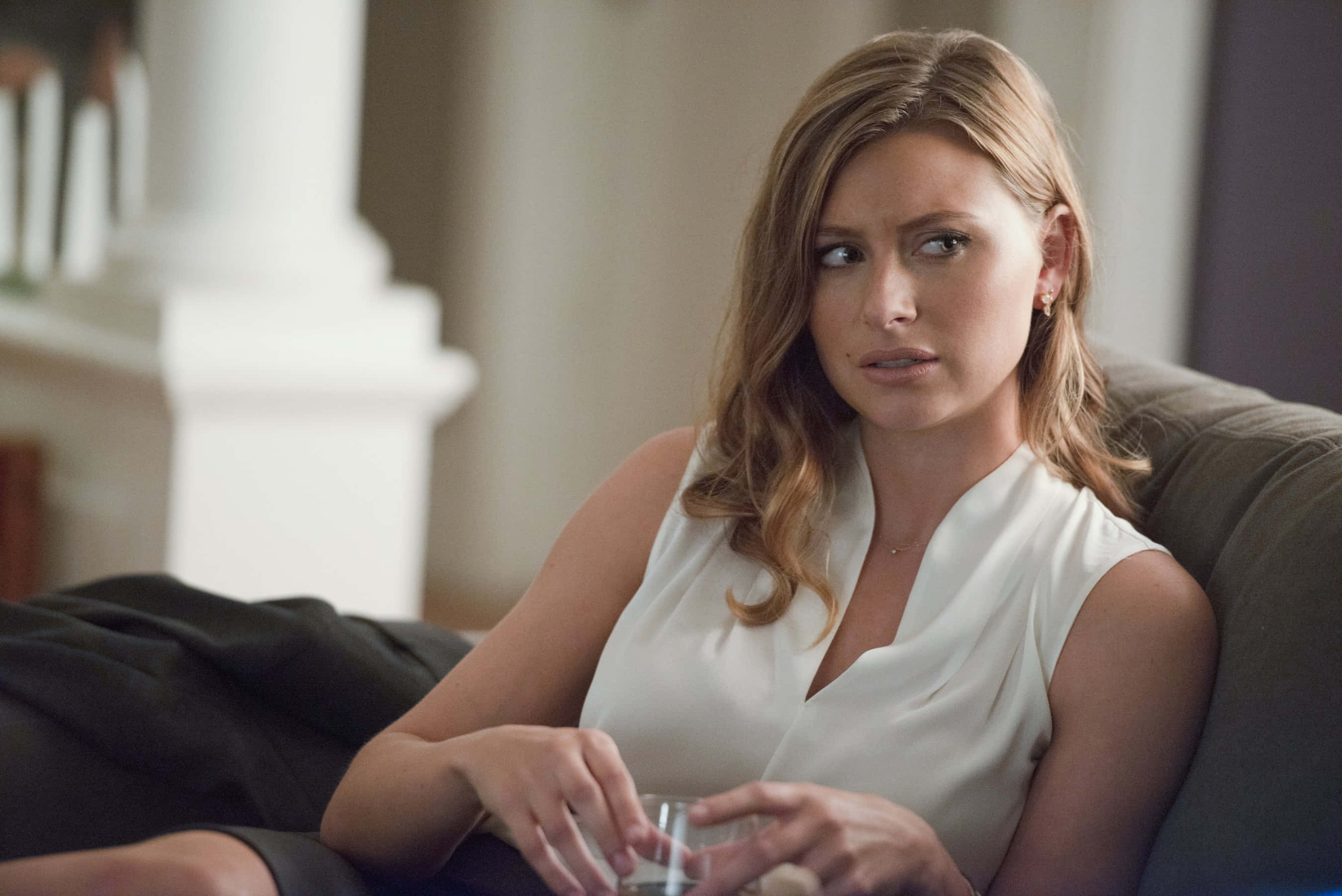 aly michalka 桌布 壁紙 — 一位身穿白色襯衫嘅女士坐喺梳化上，拎住一個杯，表情憂慮。