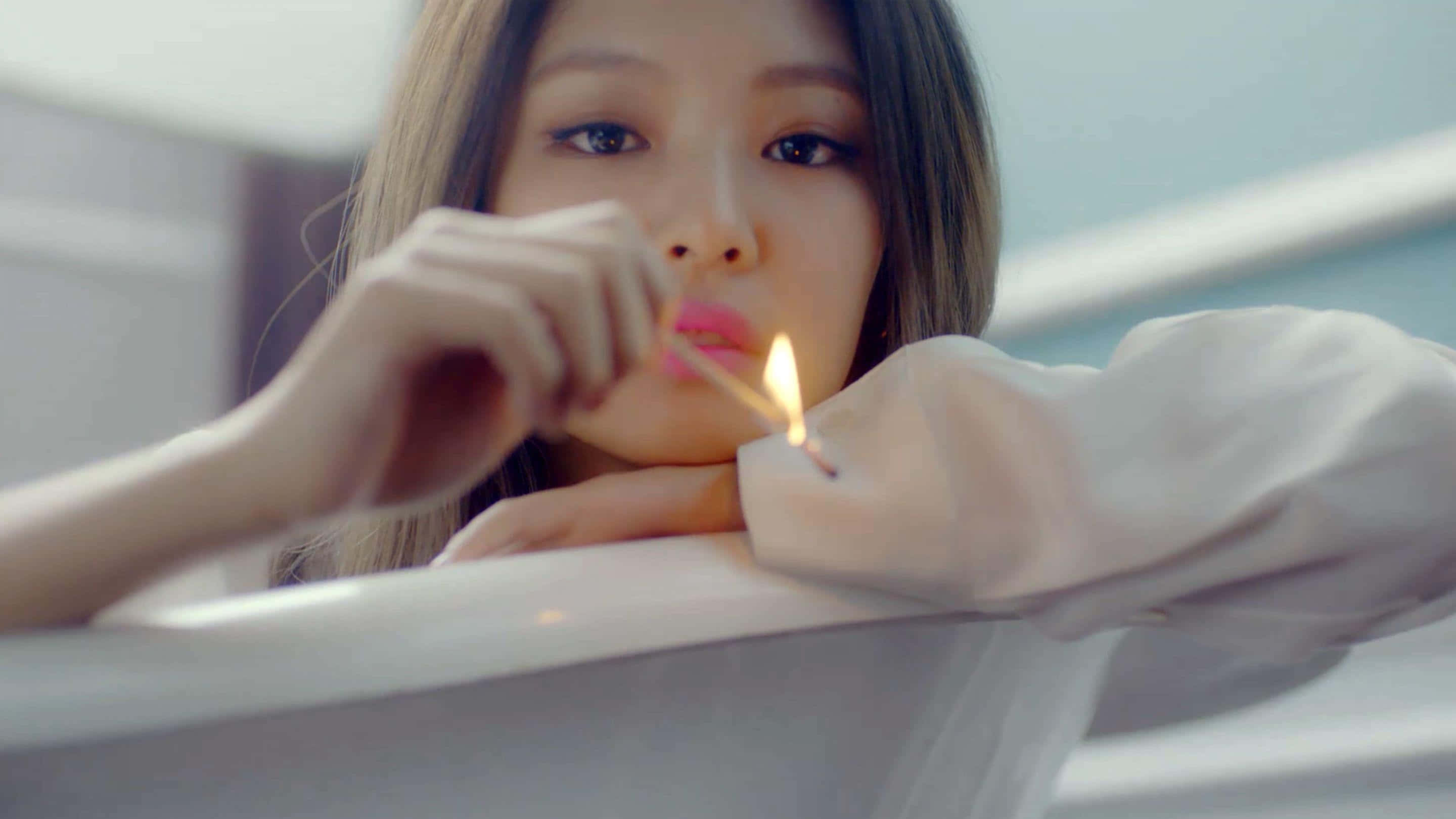 Jennie Kim 桌布 壁紙 — 一位身穿白色襯衫的年輕女性，在柔和光線的室內環境中，將點燃的火柴靠近嘴唇。