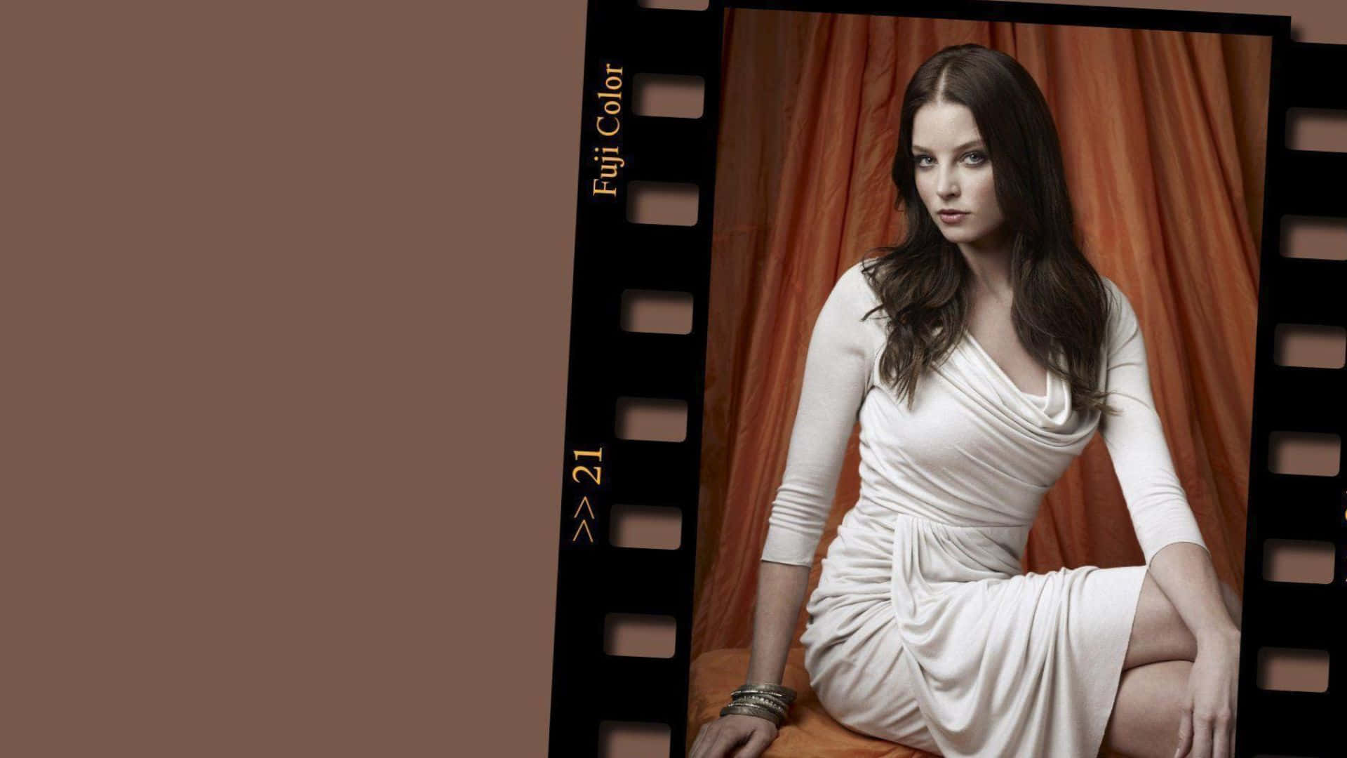 rachel nichols 桌布 壁紙 — 一位身穿白色連衣裙的女性優雅地坐在溫暖的橙色窗簾前，窗簾被黑色菲林邊框框住。