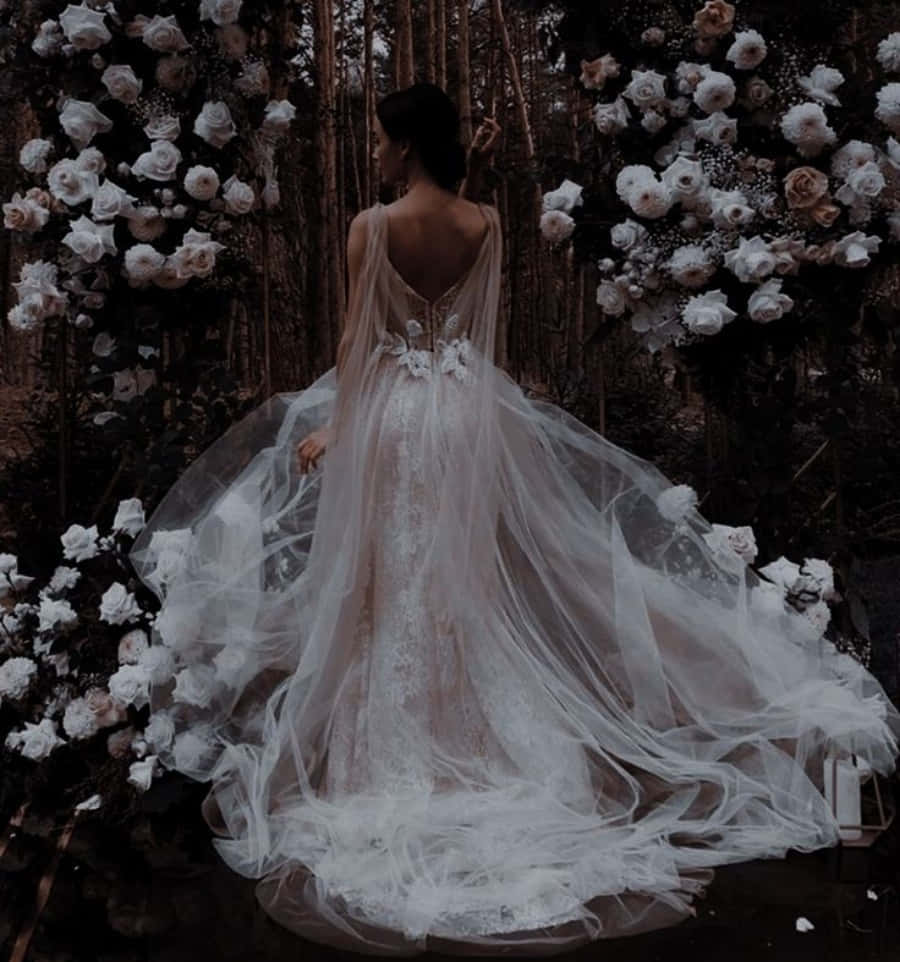 Wedding Dress 桌布 壁紙 — 一位身穿白色飄逸婚紗的新娘背對鏡頭，在黑暗的森林中被層層疊疊的白色和淡粉紅玫瑰環繞。