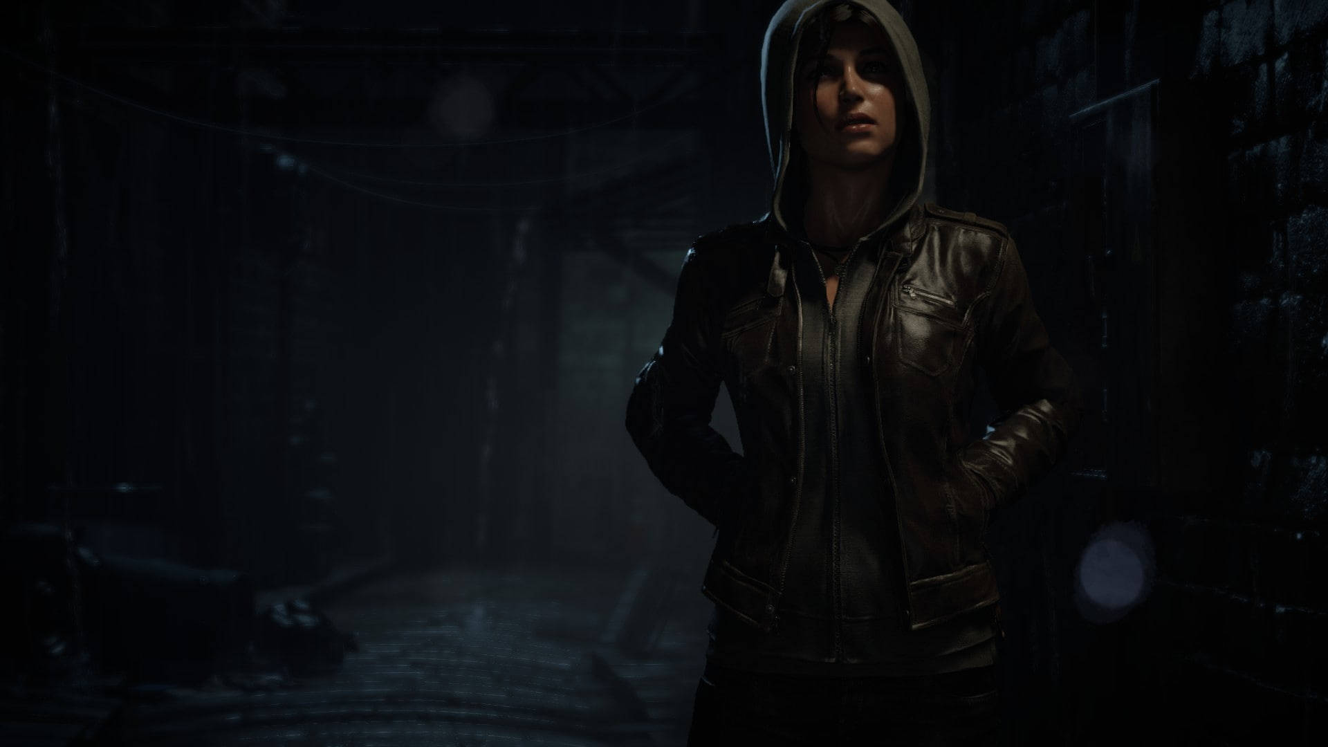 Rise Of The Tomb Raider 桌布 壁紙 — 一位身穿皮褸、戴著連帽的女子，站在昏暗有霧的後巷，四周是磚牆和懸掛的電線。