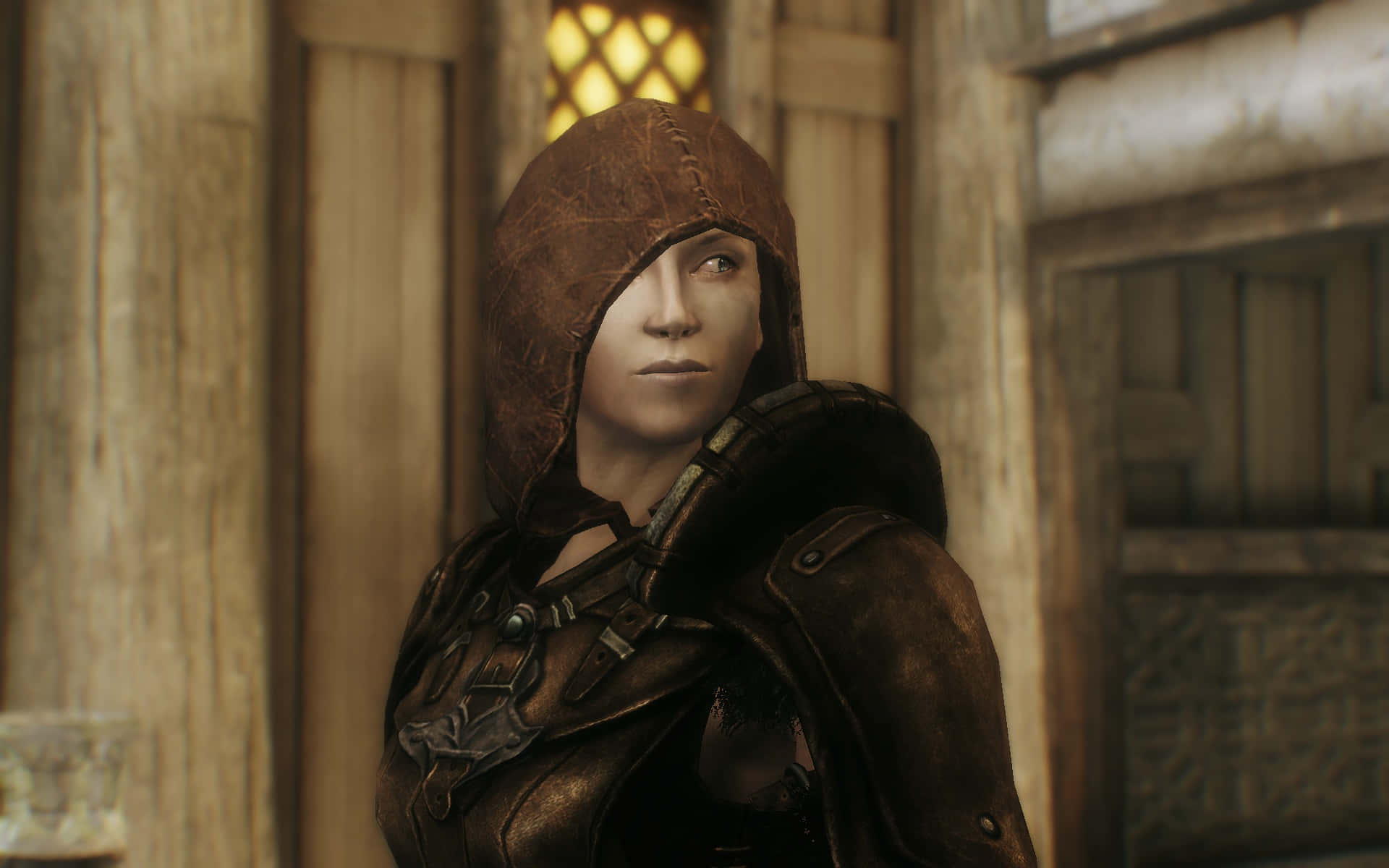 Skyrim Delphine 桌布 壁紙 — 一位身穿破舊皮甲的兜帽戰士站在質樸的木製室內，若有所思地凝視著從格子窗透進來的光線。