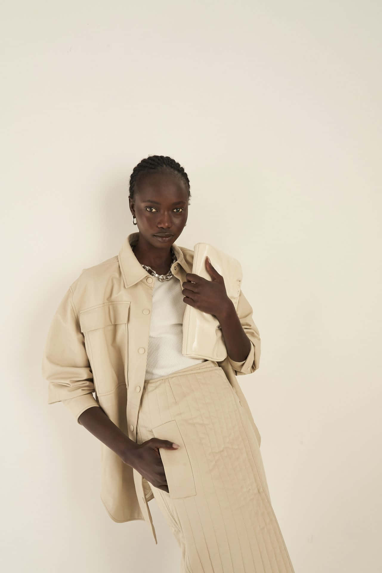 Minimalist Fashion 桌布 壁紙 — 一位身穿米色服裝的優雅女士，在純色米白工作室背景前拿著一個相配的手拿包。