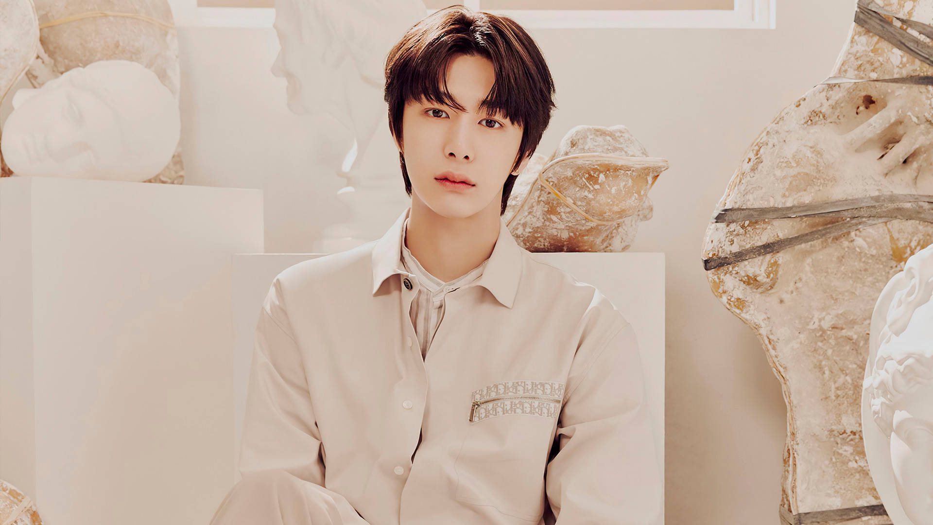 Monsta X Hyungwon Fantasia X 壁紙 — 一位身穿米色襯衫的年輕男子在柔和光線的工作室中，靜靜地坐在白色大理石雕塑之間。