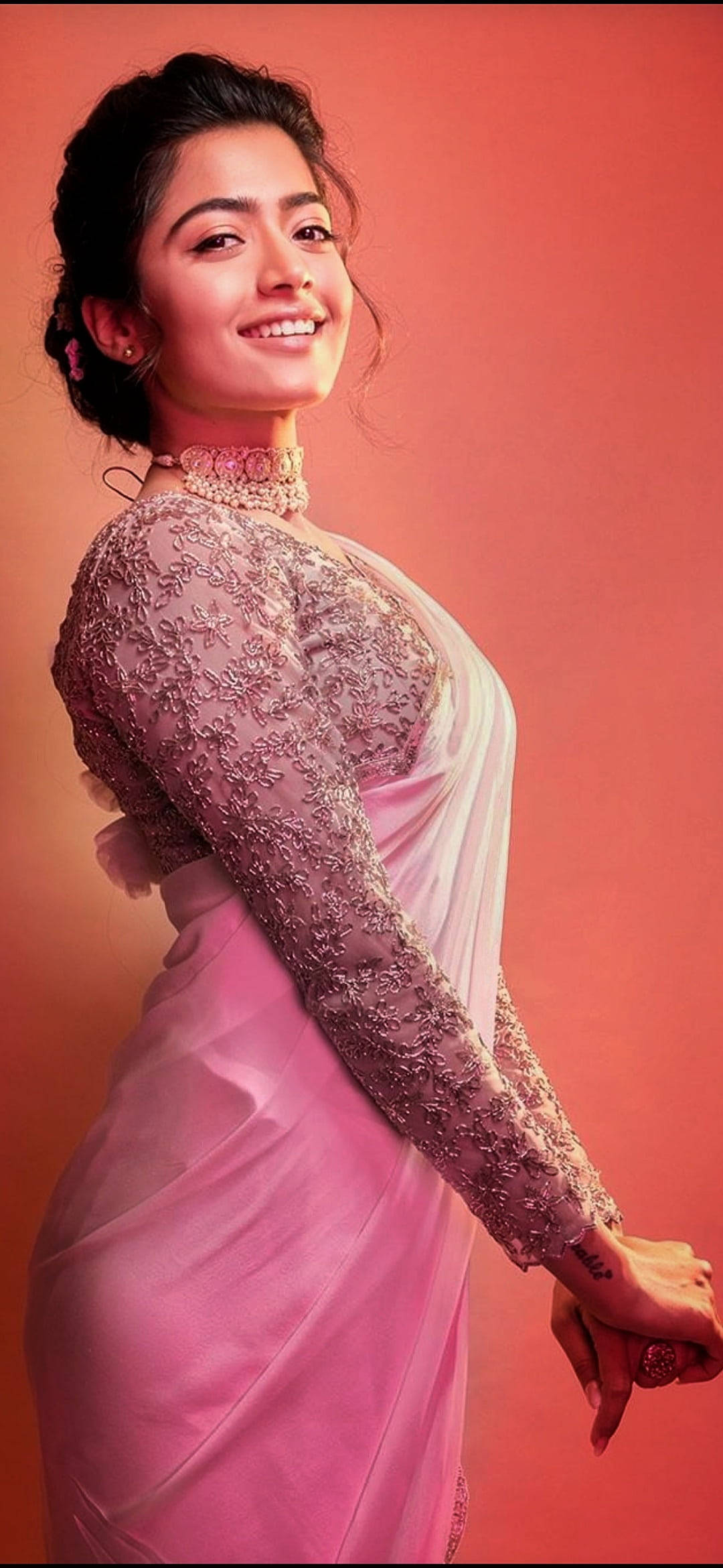 telugu 桌布 壁紙 — 一位身穿粉紅色刺繡紗麗的女性在純珊瑚色背景前溫暖微笑。