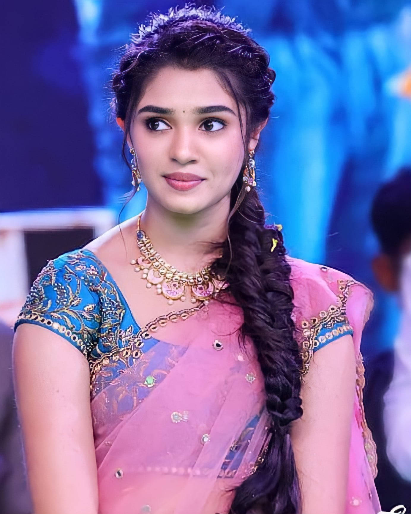 telugu 桌布 壁紙 — 一位身穿粉藍色刺繡紗麗、留著長辮子的年輕女子，在模糊的藍色舞台背景下若有所思地凝視著。