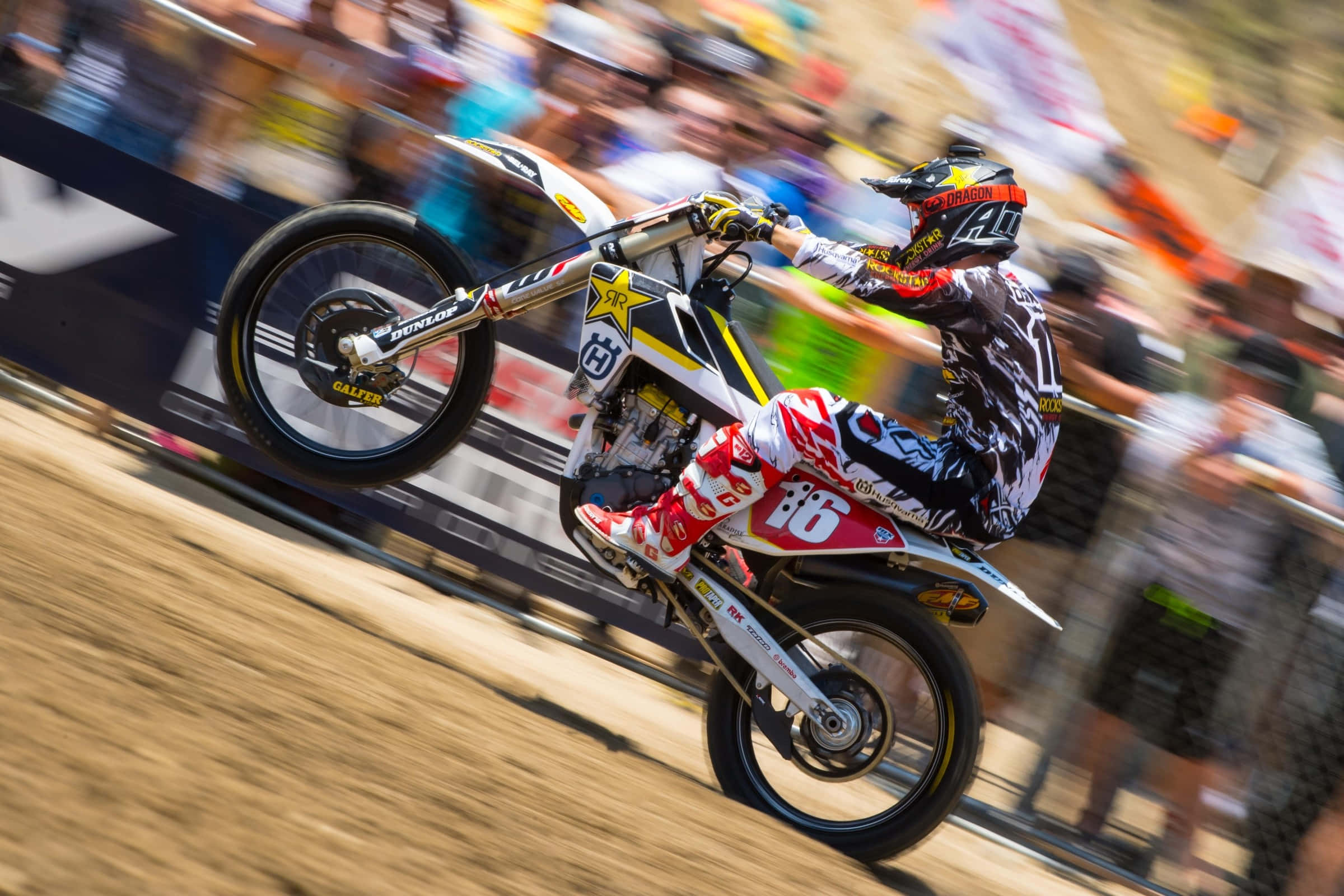 Motocross 桌布 壁紙 — 一位身穿紅、白、黑色裝備的越野電單車手在泥地賽道上傾斜入彎，背景有模糊的觀眾。