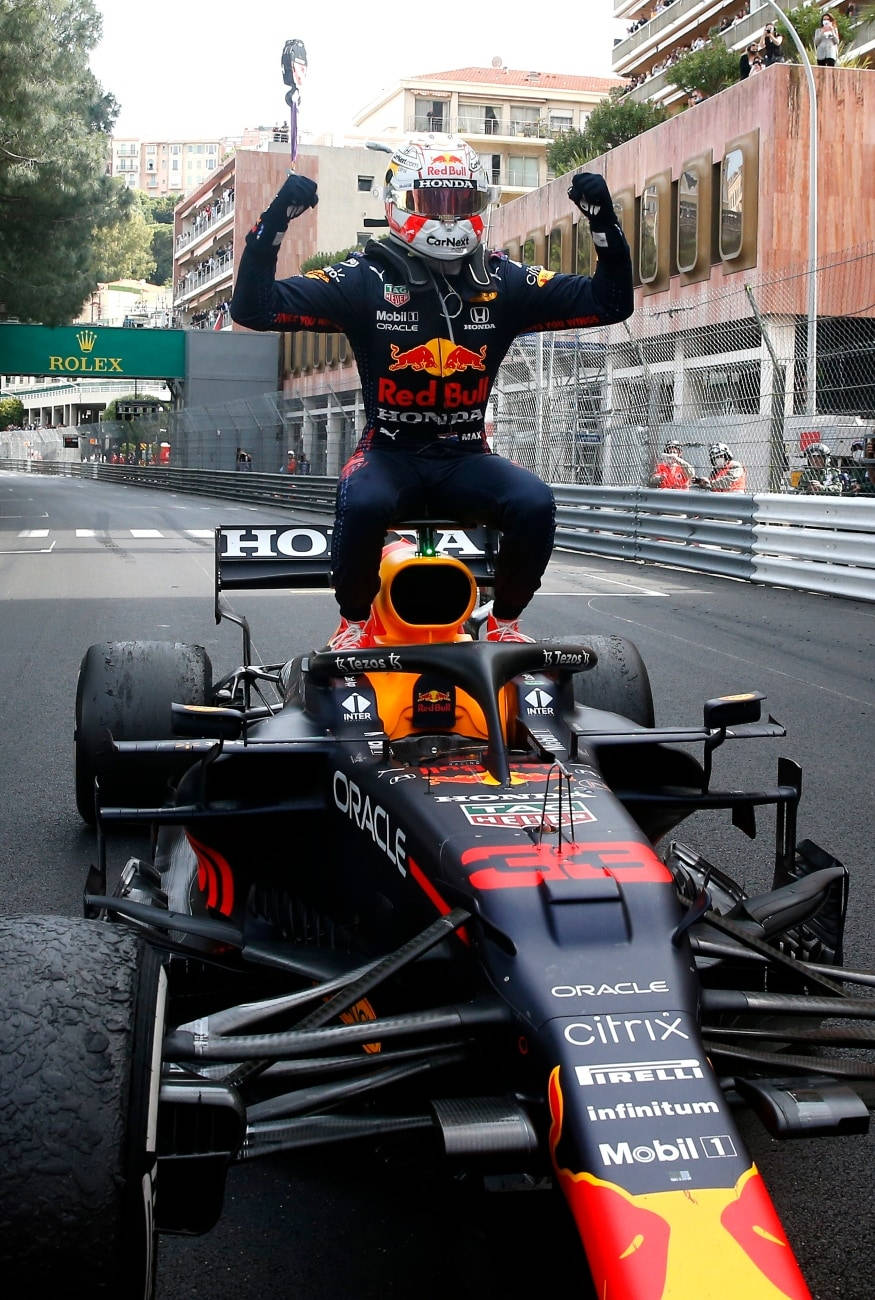 Verstappen 桌布 壁紙 — 一位身穿紅牛賽車服的F1車手，在陽光明媚的街道賽道上，坐在他的黑色和橙色賽車上慶祝勝利。