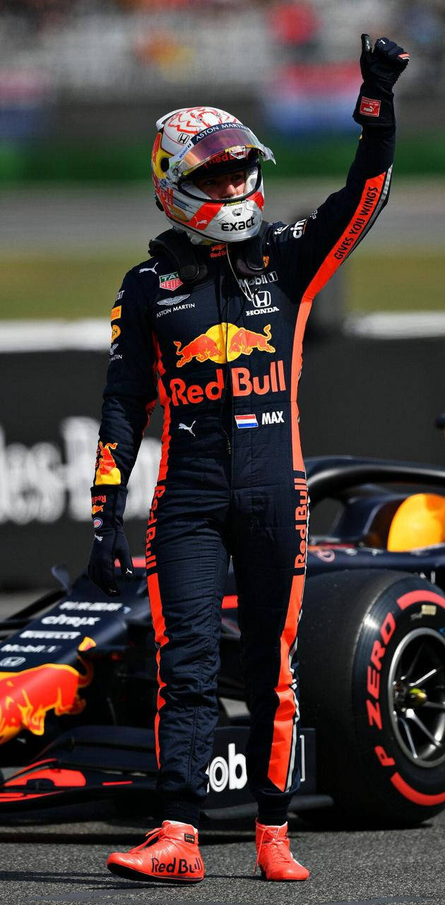 Verstappen 桌布 壁紙 — 一位身穿紅牛賽車服的F1車手在賽道上舉起一隻手臂，在他的賽車旁慶祝勝利。