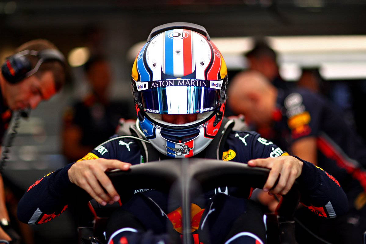 F1 桌布 壁紙 — 一位身穿紅牛車隊頭盔和賽車服的F1車手在車房內握著賽車的方向盤。