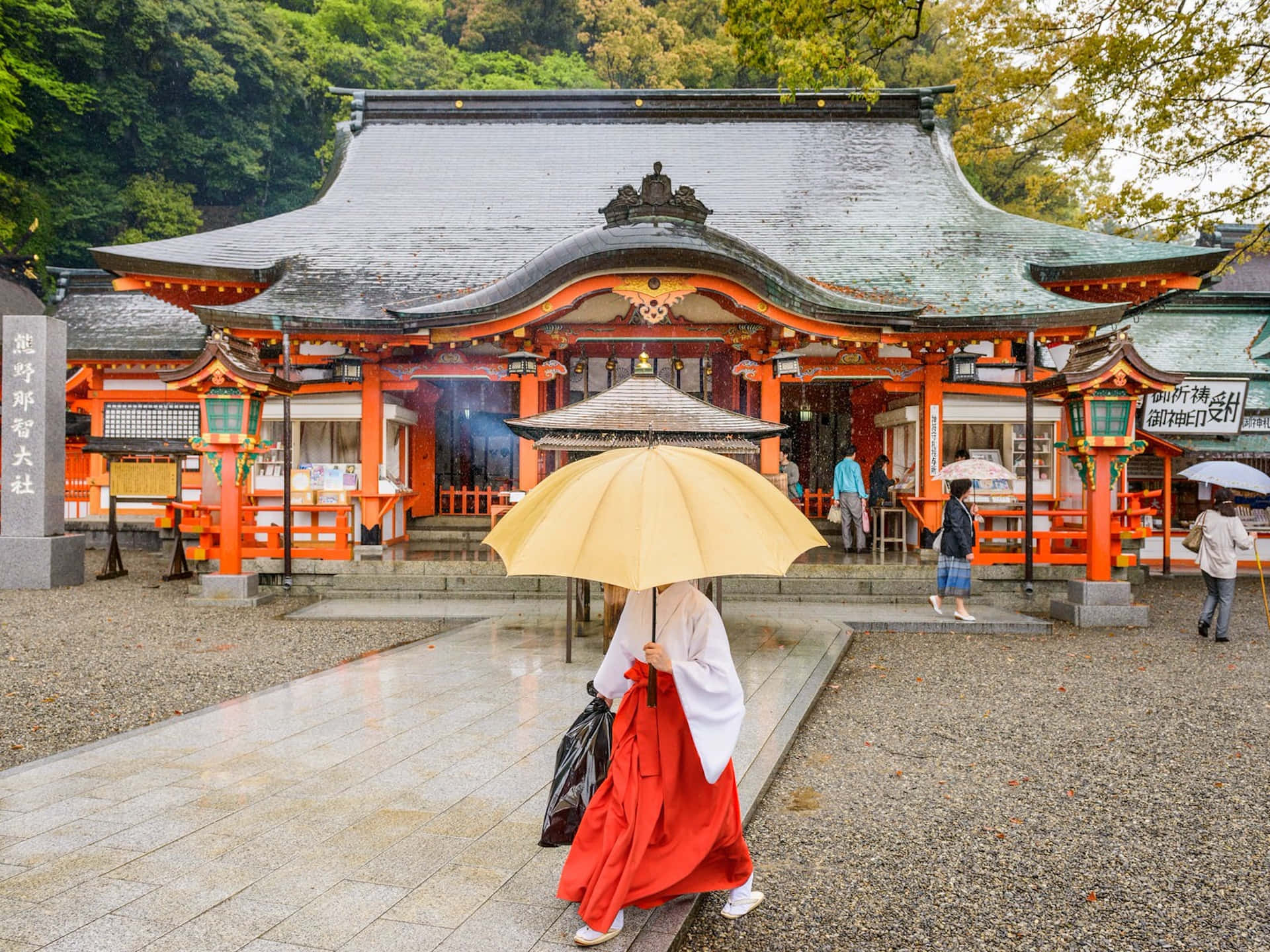 Japanese 桌布 壁紙 — 一位身穿紅白和服的人撐著黃色雨傘，走向一座擁有橙色柱子和綠色屋頂的傳統日本神社。