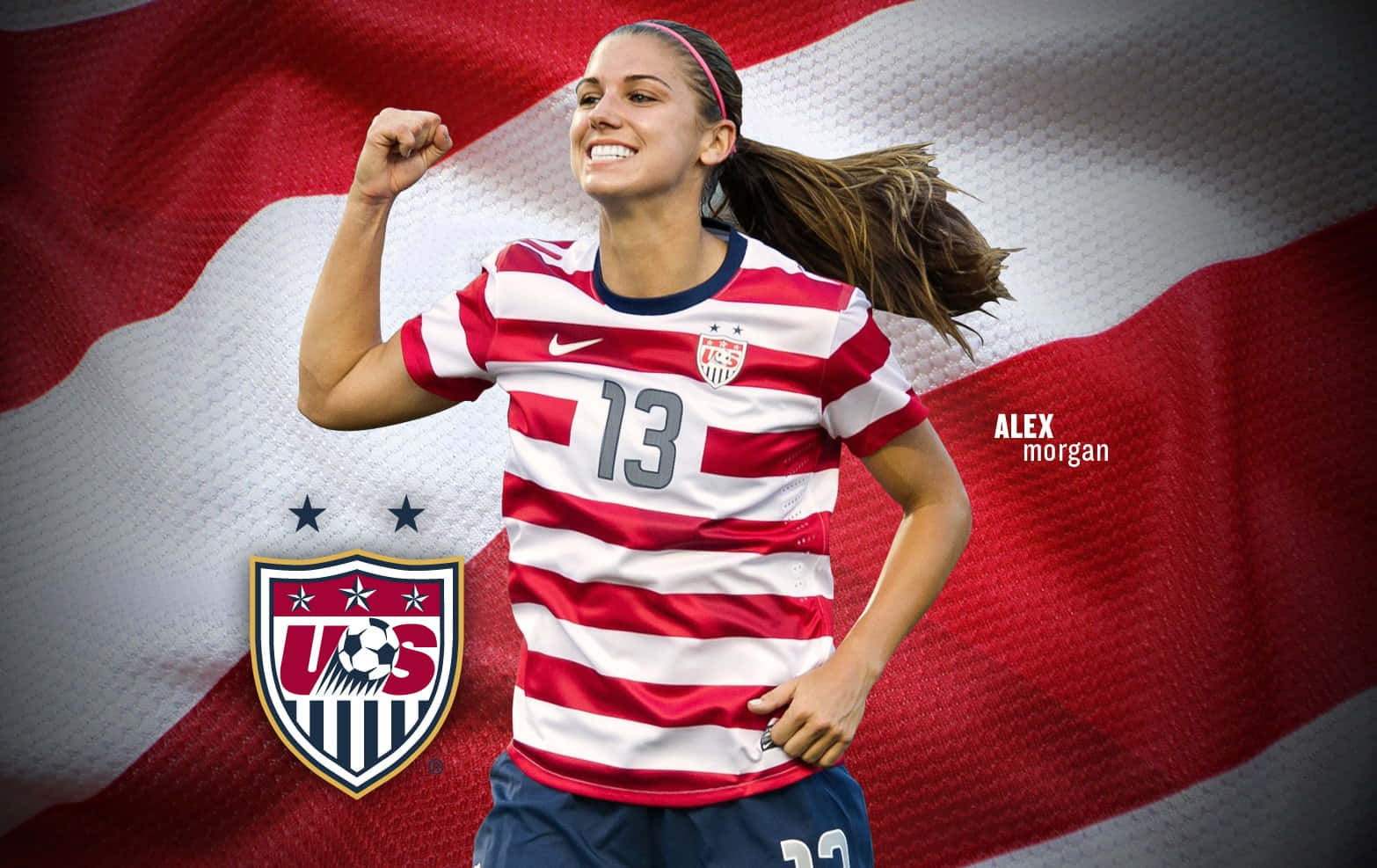Alex Morgan 桌布 壁紙 — 一位身穿紅白條紋球衣的美國足球員，在飄揚的美國國旗背景下握緊拳頭慶祝勝利。
