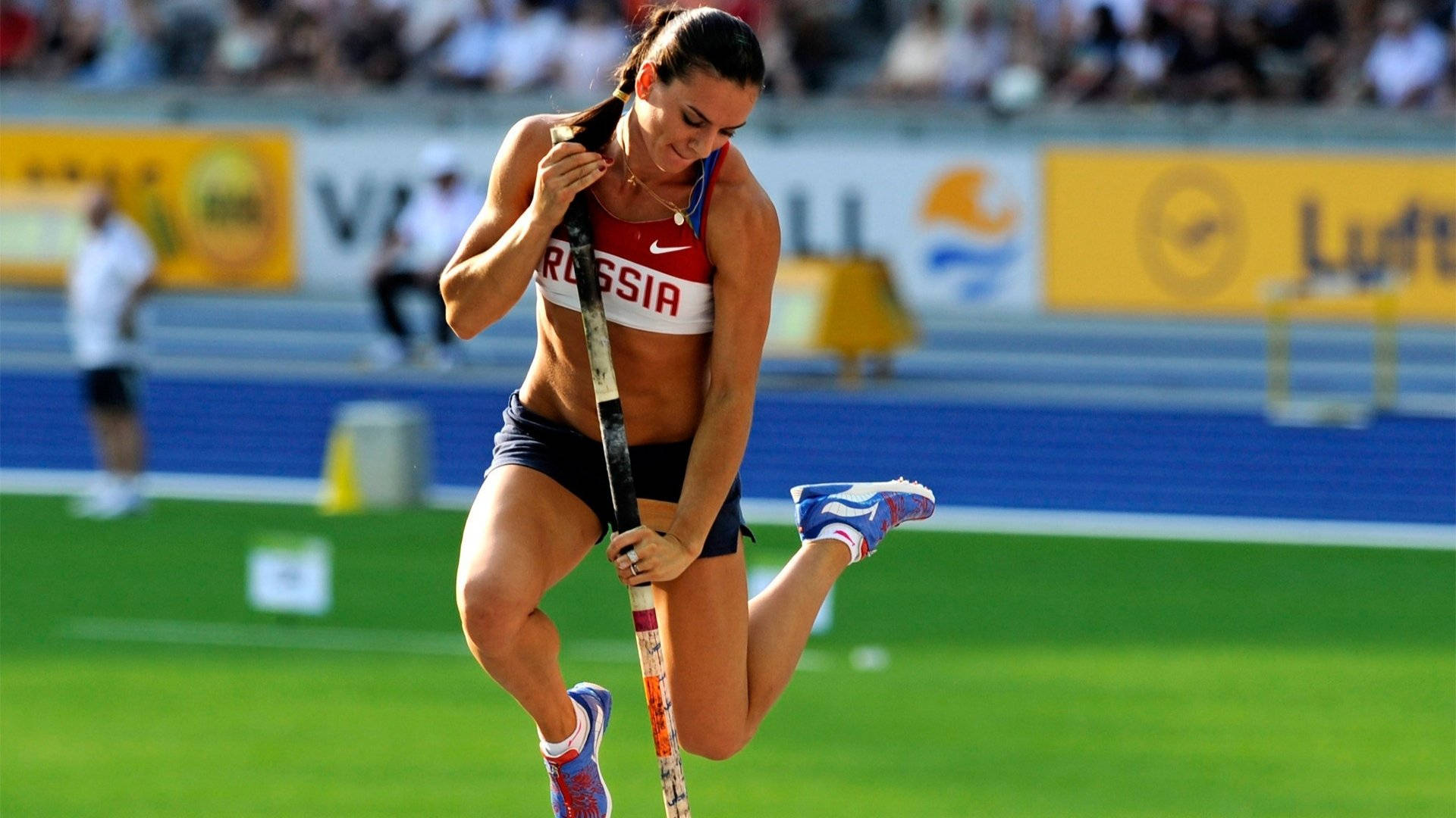 運動 桌布 壁紙 — 一位身穿紅白藍裝備的俄羅斯女子撐竿跳運動員，在明亮的日光下於綠色跑道上準備跳躍。