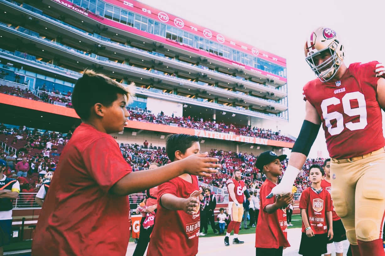 Mike Mcglinchey 桌布 壁紙 — 一位身穿紅色69號球衣的三藩市四九人美式足球員在擠滿觀眾的球場上向年輕球迷打招呼。