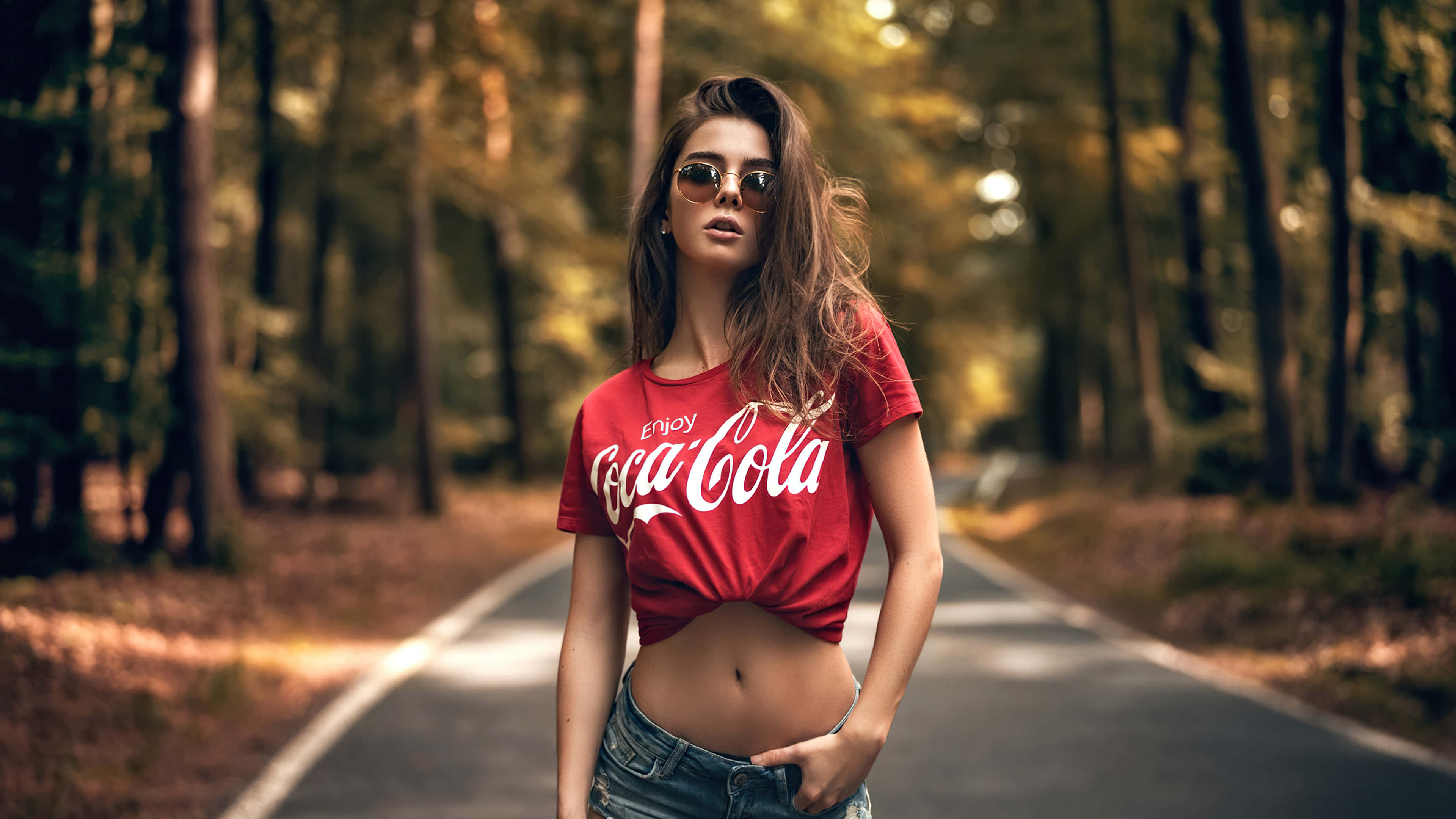 一位身穿紅色可口可樂上衣的女性站在路上 壁紙