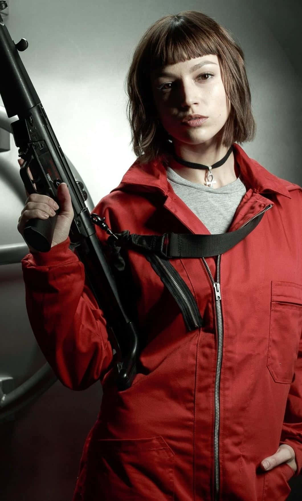 Money Heist 桌布 壁紙 — 一位身穿紅色外套的女性，在灰色攝影棚背景下，表情嚴肅地拿著步槍。
