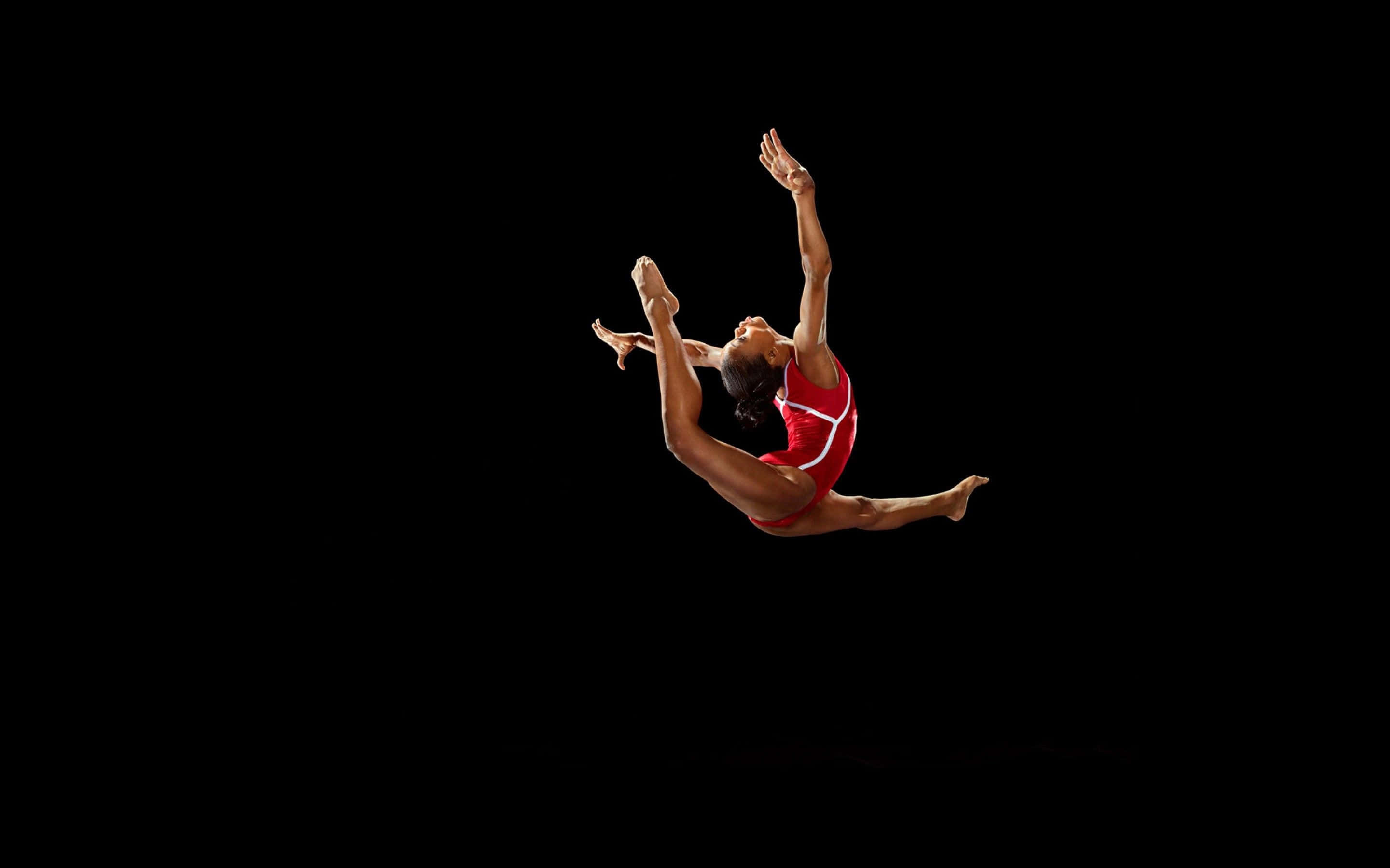 Gymnastics 桌布 壁紙 — 一位身穿紅色緊身衣的女體操運動員在純黑背景上做出動態空中劈腿動作。