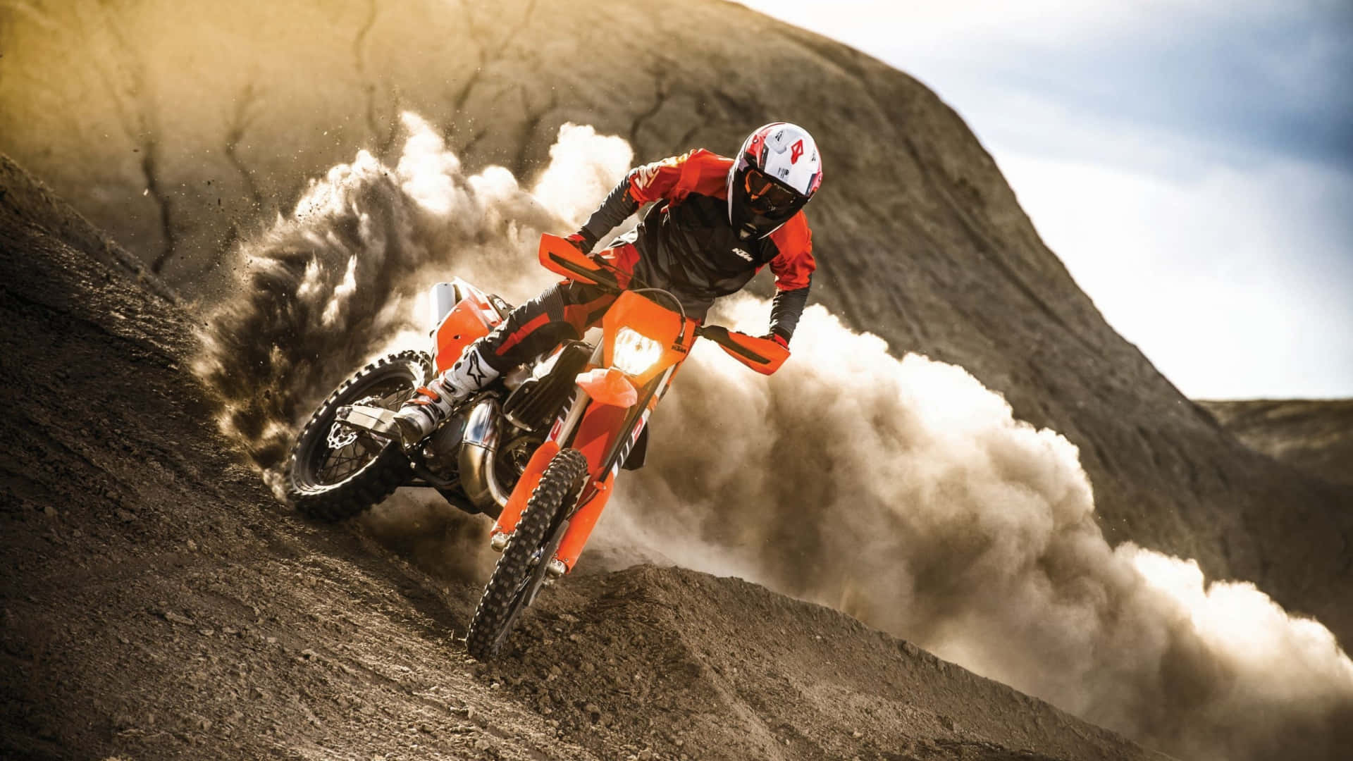 Motocross 桌布 壁紙 — 一位身穿紅色裝備的越野電單車手在橙色電單車上傾斜入彎，在崎嶇的泥坡上揚起灰塵，陽光普照。