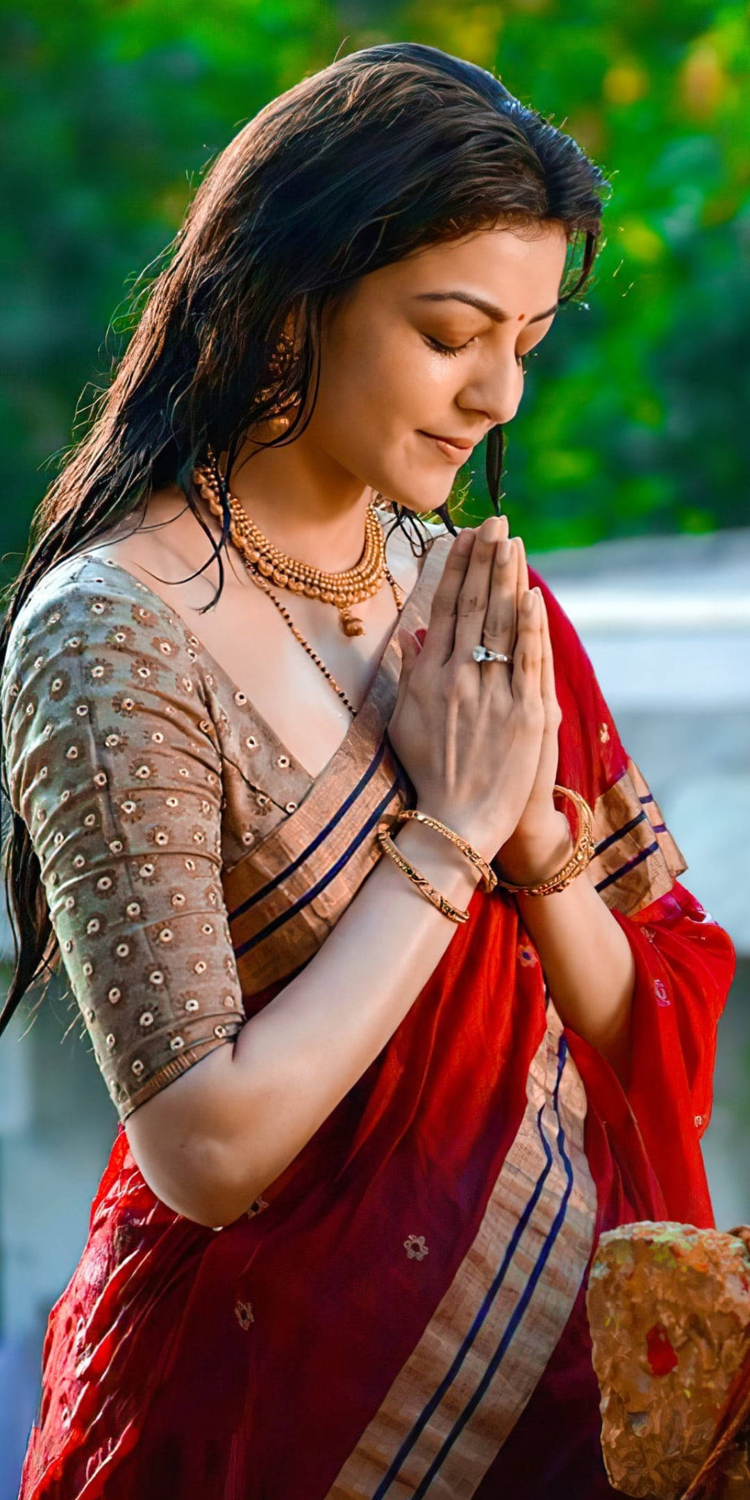 Indian 桌布 壁紙 — 一位身穿紅金色紗麗的女性，在戶外雙手合十、閉目祈禱，神情寧靜虔誠。