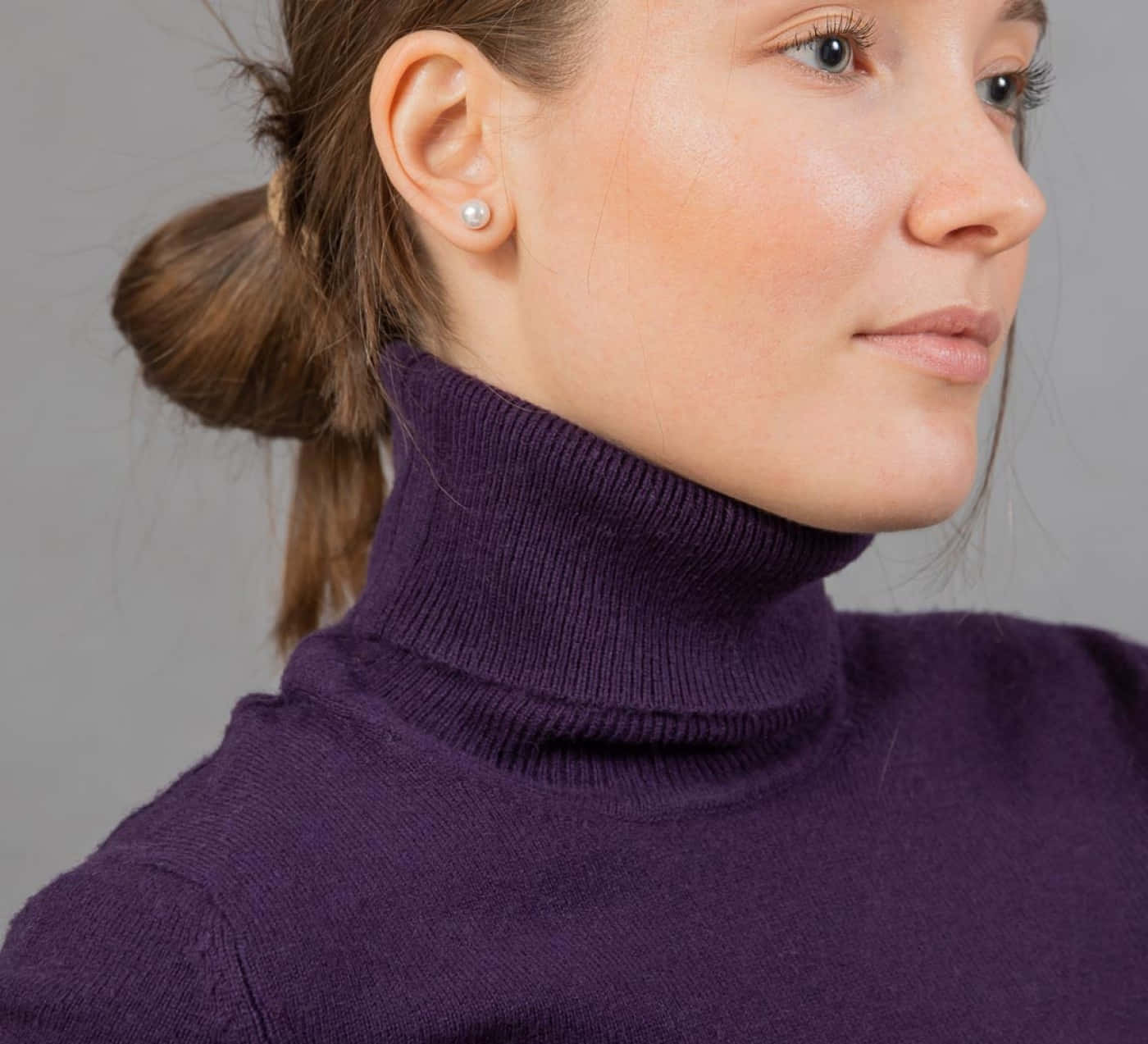 Purple Turtle-neck Sweater 桌布 壁紙 — 一位身穿紫色高領毛衣、戴著珍珠耳環的女性，在灰色中性背景前的特寫。
