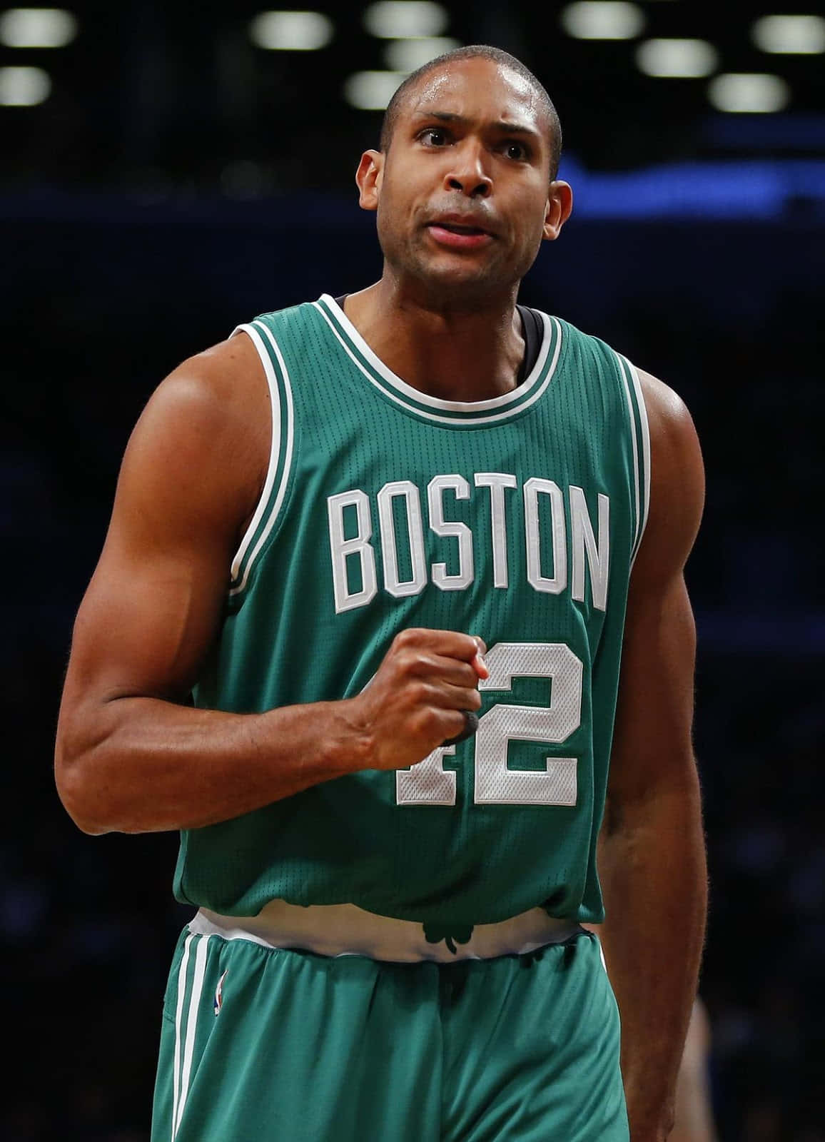 Al Horford 桌布 壁紙 — 一位身穿綠色波士頓球衣、背號22的專注籃球運動員，在場館燈光下於比賽中握緊拳頭。