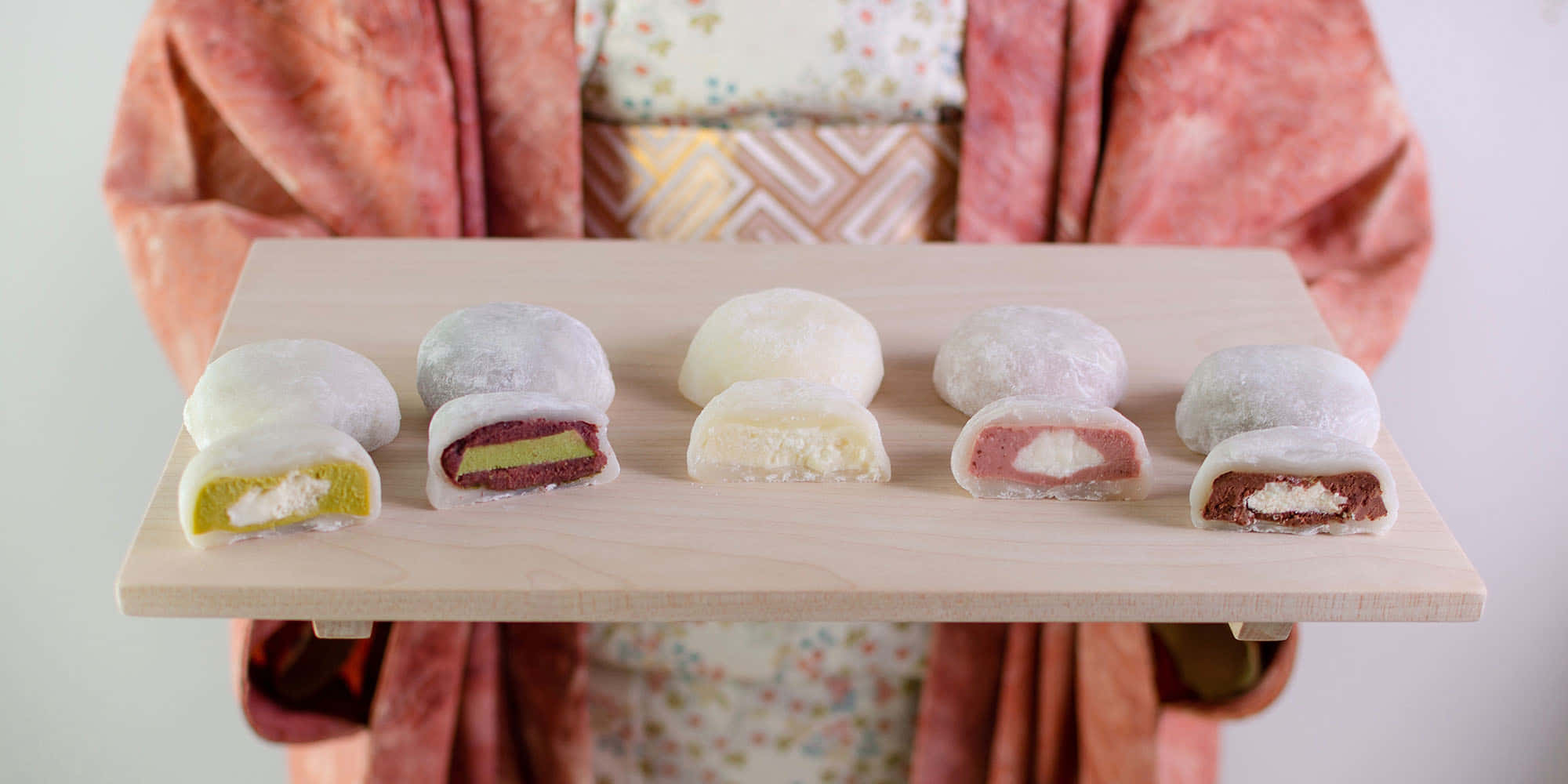 Japanese Sweets 桌布 壁紙 — 一位身穿花卉和服的人手持一個木托盤，上面有六個切半的麻糬，露出色彩繽紛的甜味餡料。