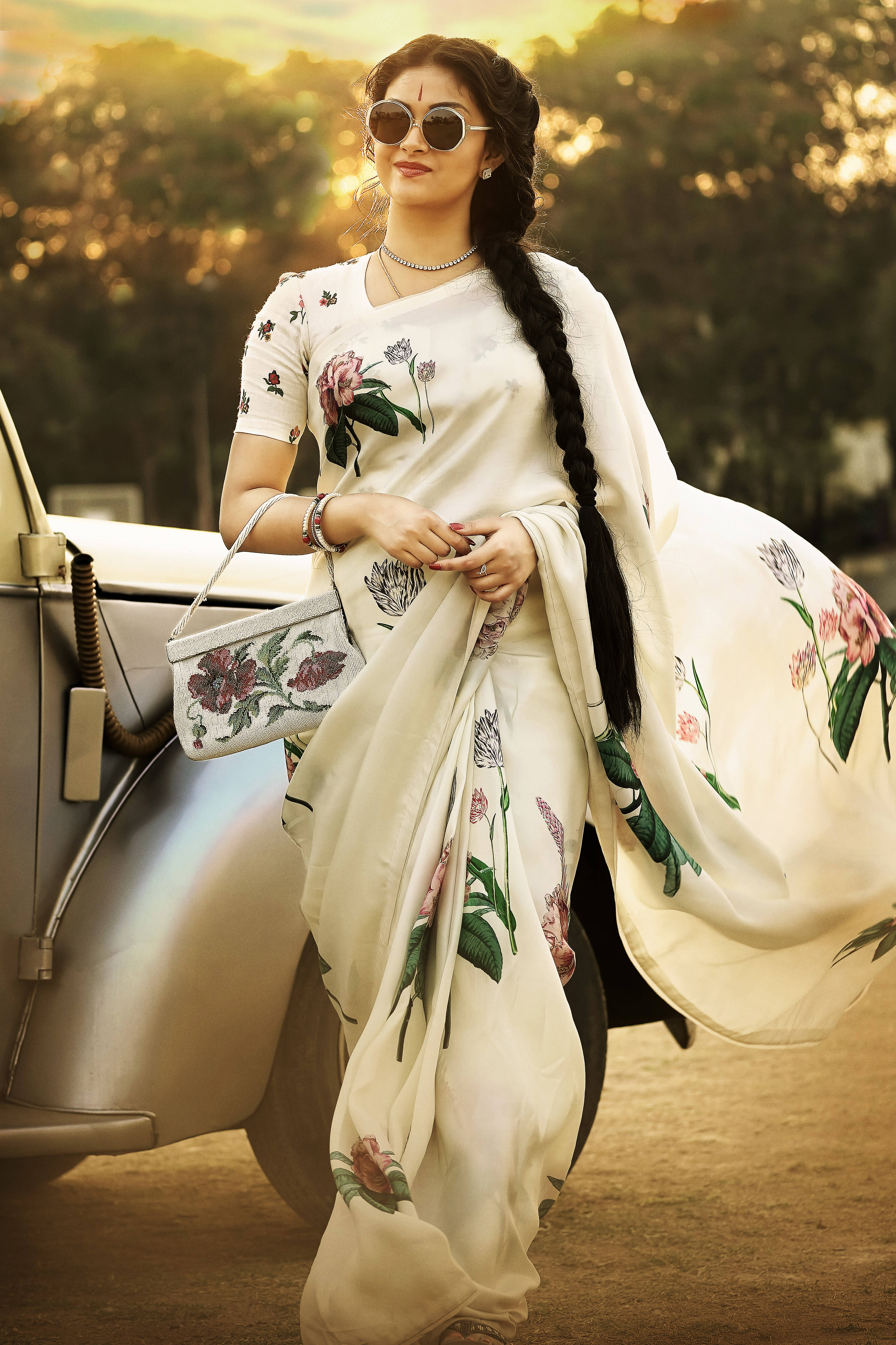 Indian 桌布 壁紙 — 一位身穿花卉白色紗麗的女性站在一輛復古車旁，金色夕陽的光芒灑在她和身後的樹木上。